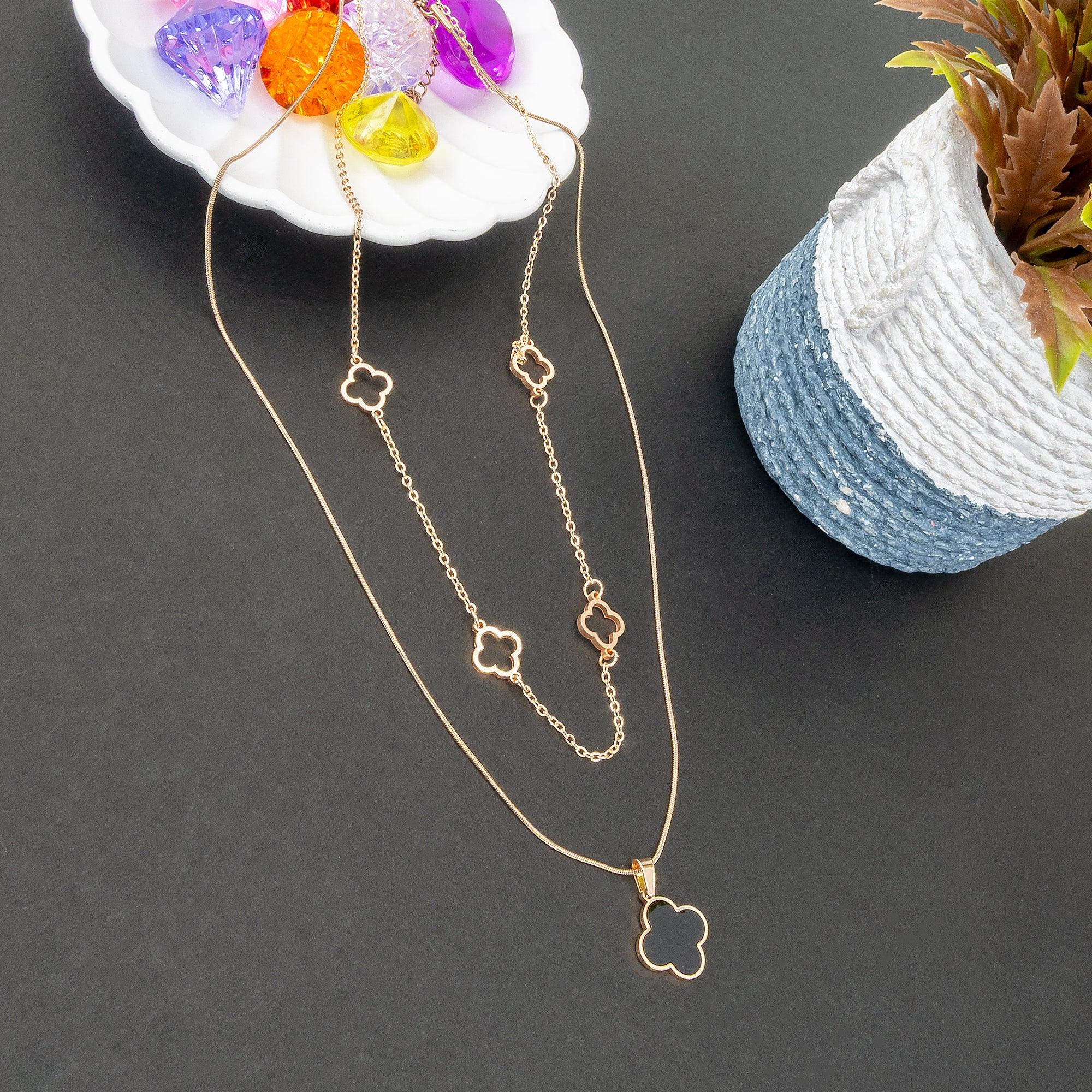 Gold necklace with clover pendants on a dark surface with a plant and colorful beads in the background.