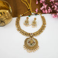 Gold necklace and earrings on a white surface with a gold cup and pink flowers in the background.