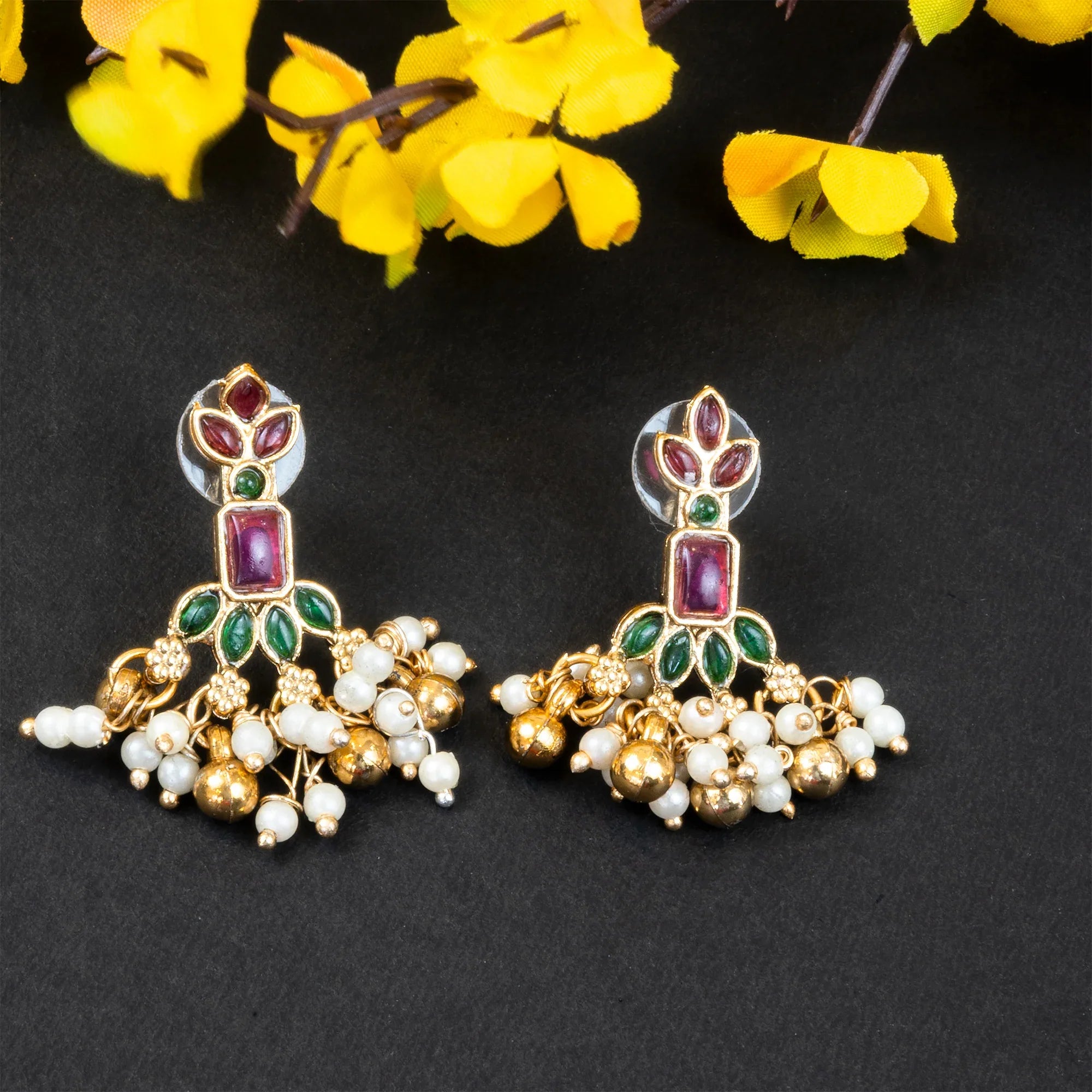 Ornate earrings with gemstones and pearls on a dark background with yellow flowers.