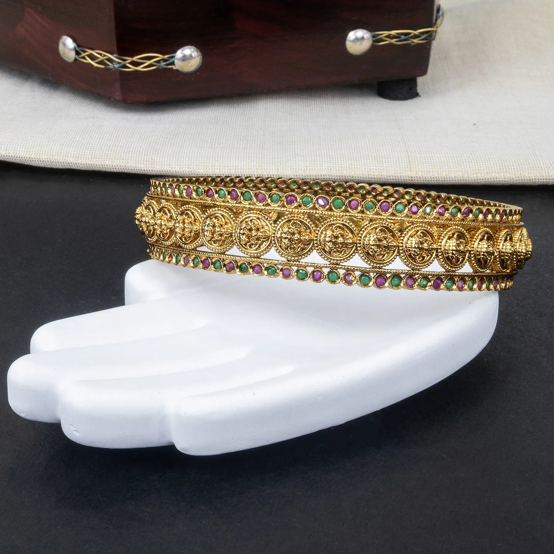 Gold anklets with gemstones on a white foot model against a dark background