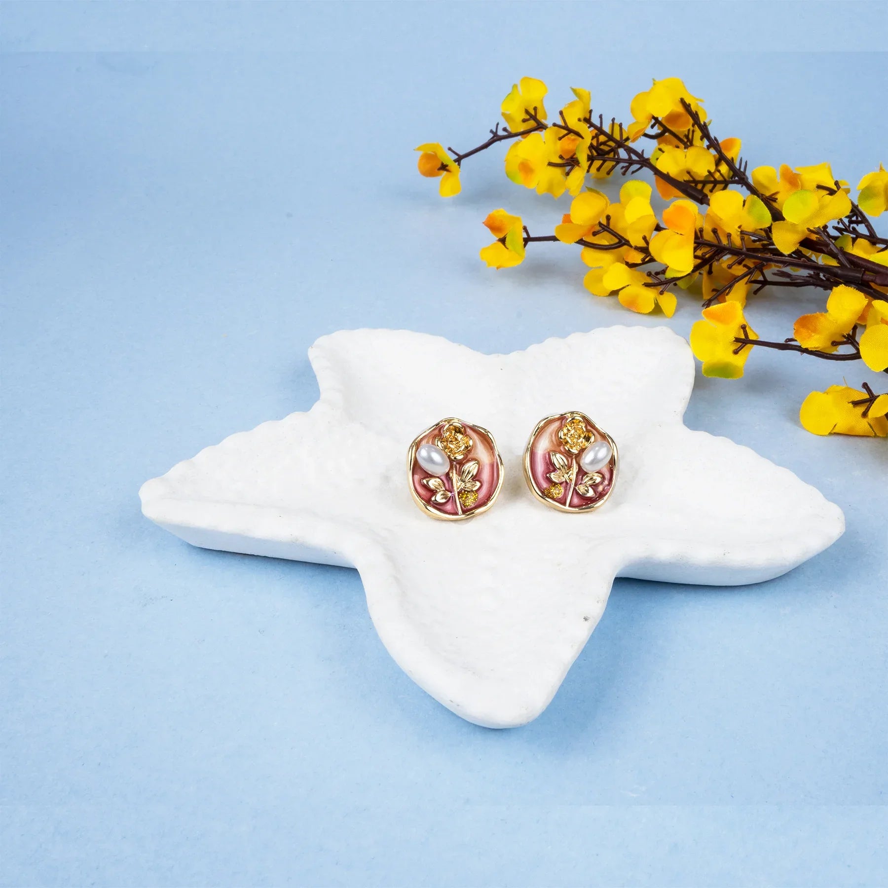 Pair of earrings on a star-shaped white stand with yellow flowers on a light blue background
