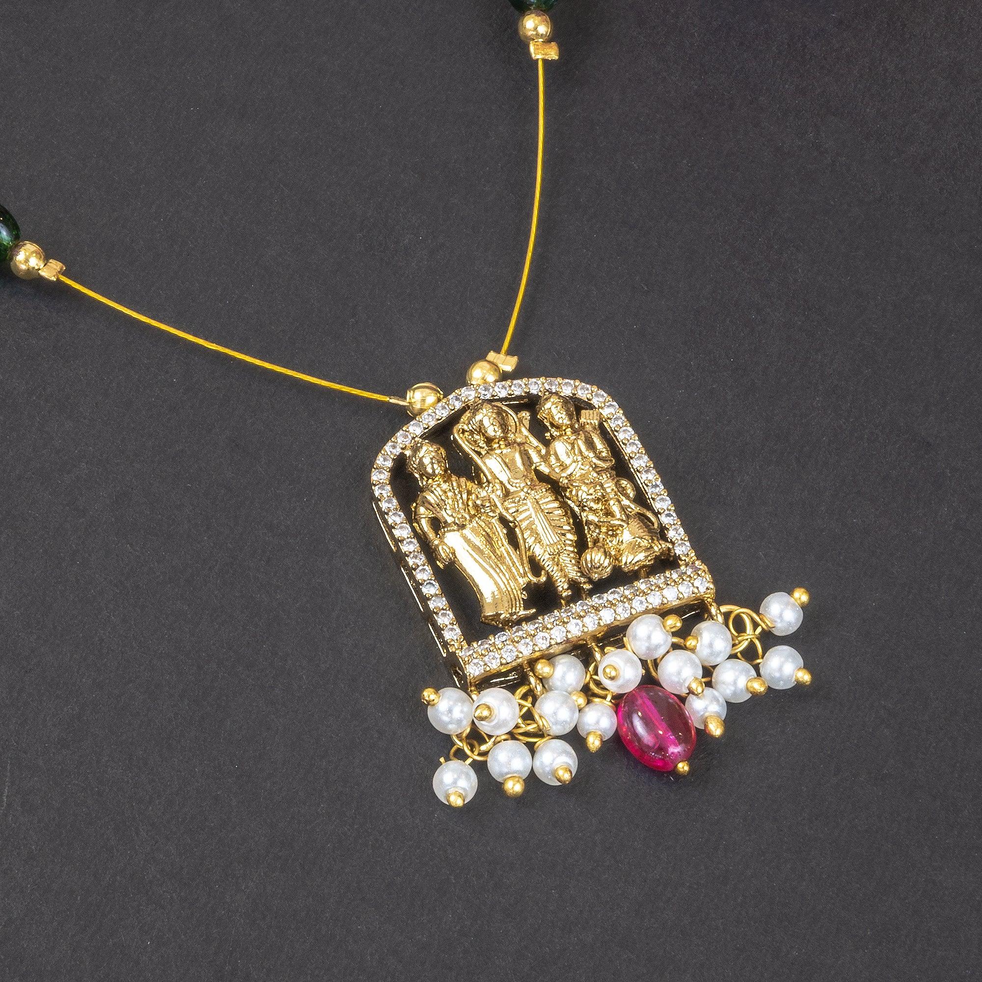 Decorative pendant with gold figures, pearls, and a red gemstone on a dark background