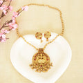 Gold necklace and earrings set on a white shell with pink flowers in the background