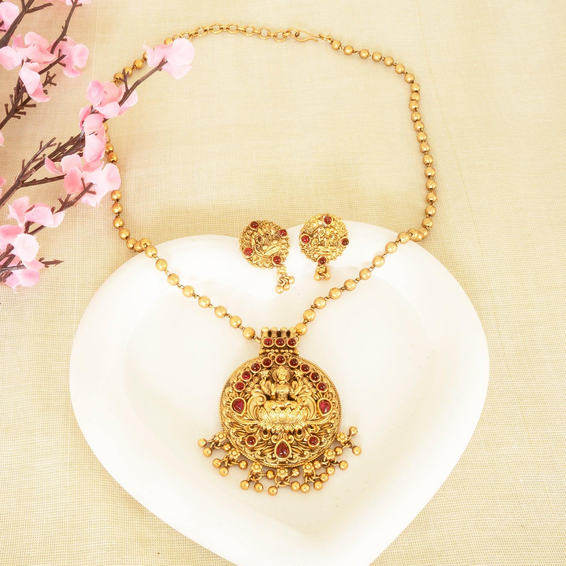 Gold necklace and earrings set on a white shell with pink flowers in the background