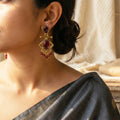 Close-up of a woman wearing gold earrings with red gemstones, wearing a black saree.
