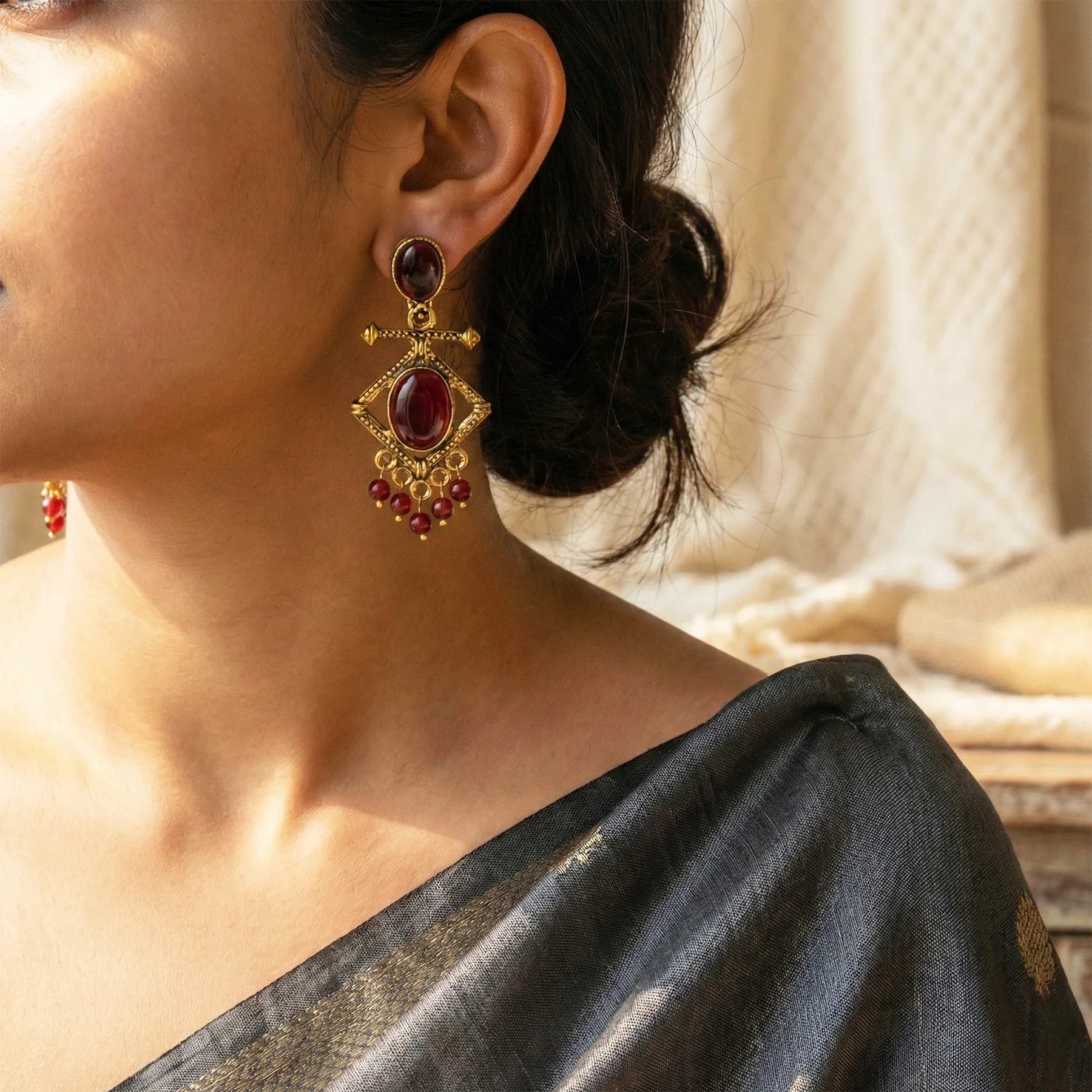 Close-up of a woman wearing gold earrings with red gemstones, wearing a black saree.