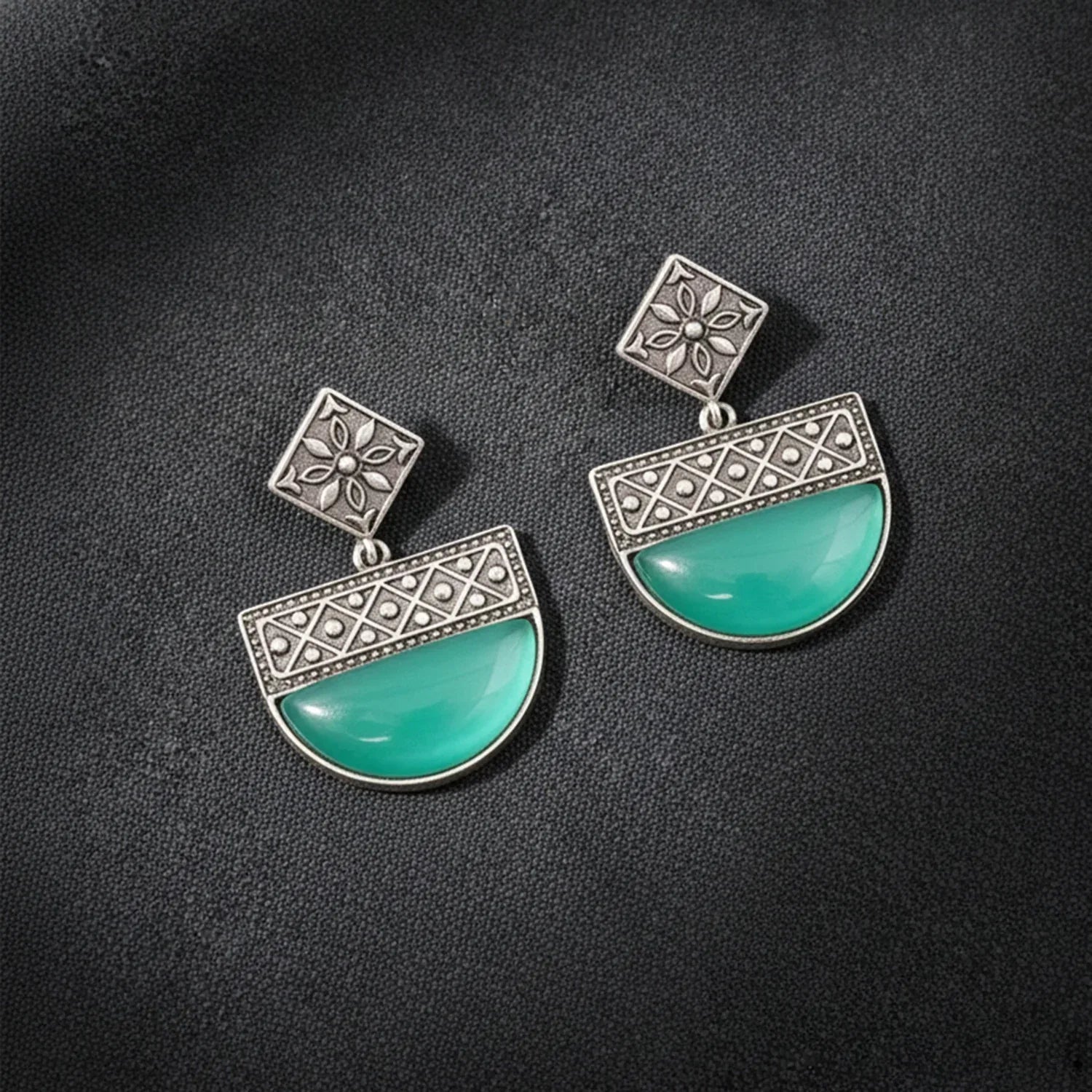 Pair of earrings with turquoise stones and silver floral designs on a dark background