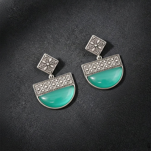 Pair of earrings with turquoise stones and silver floral designs on a dark background