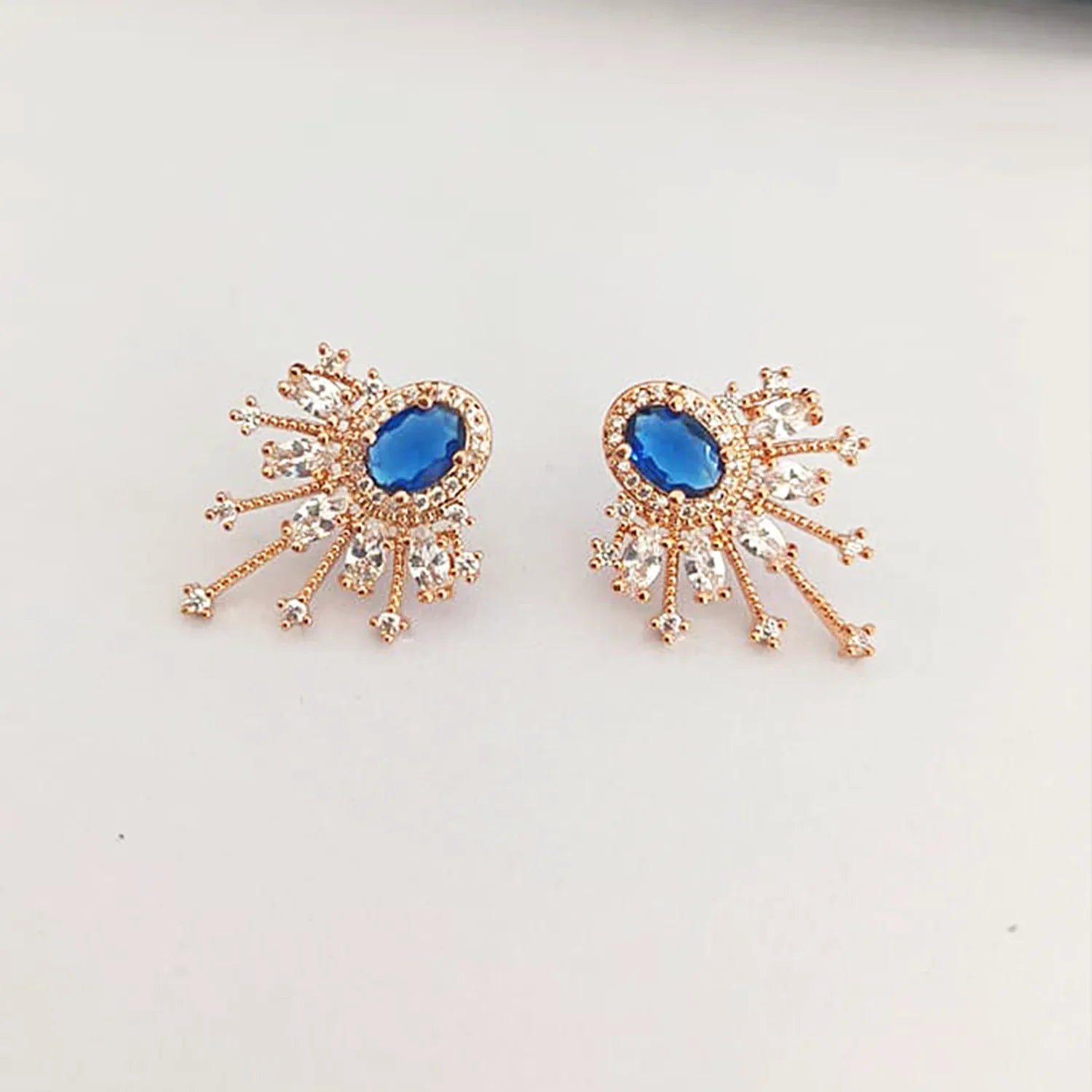 Pair of earrings with blue gemstones and rose gold accents on a light gray background