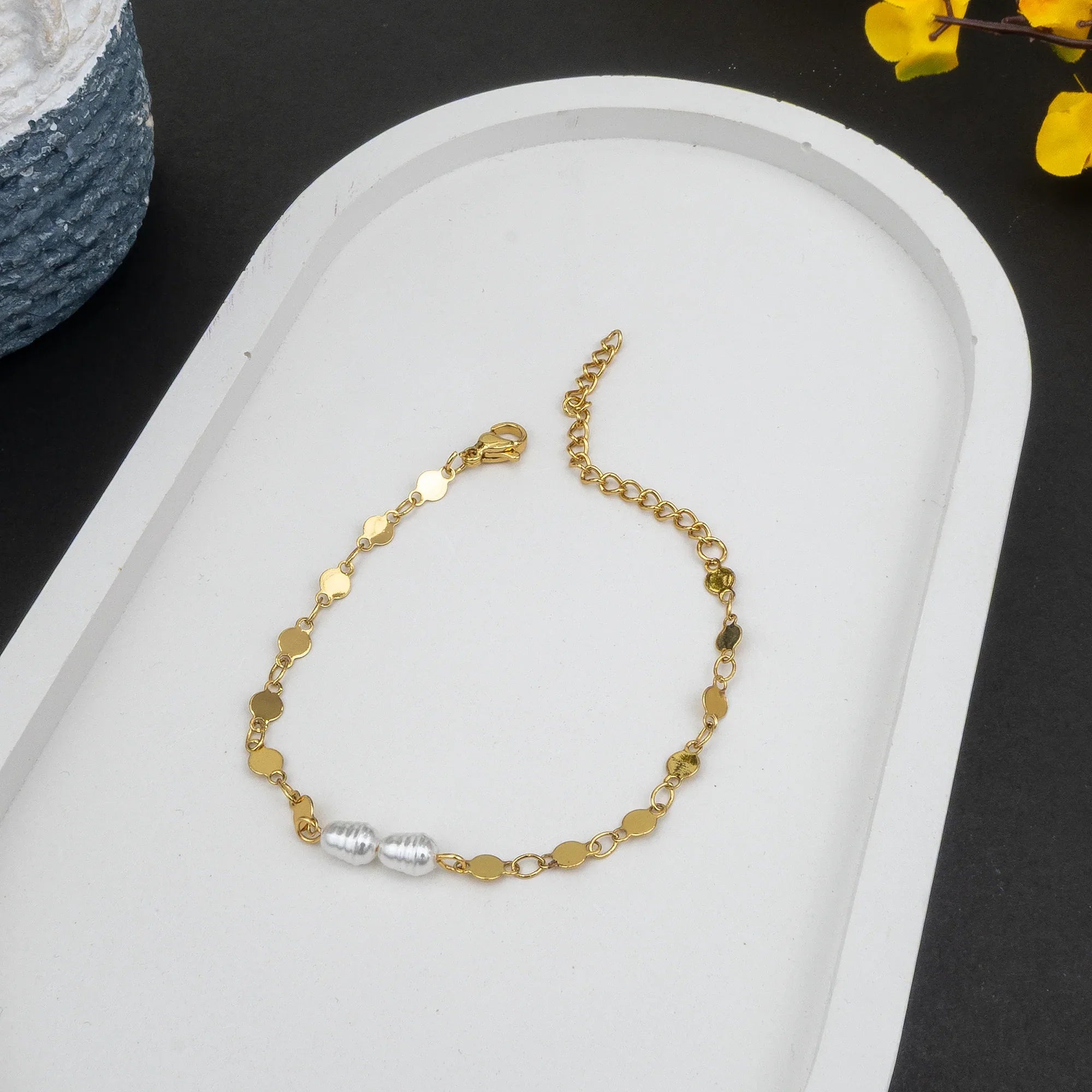 Gold bracelet with a silver clasp on a white tray with a black background