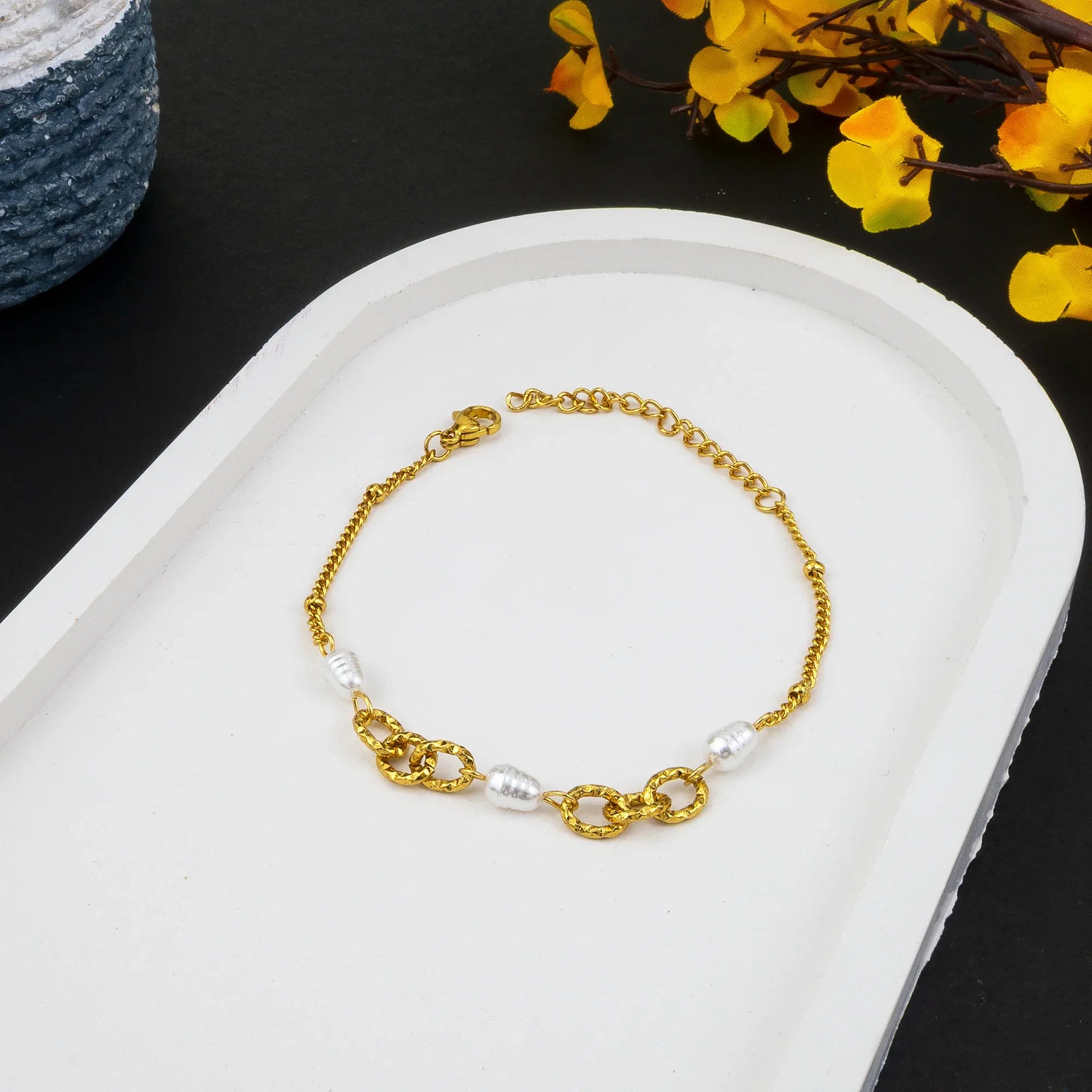 Gold bracelet with pearls on a white dish with yellow flowers in the background