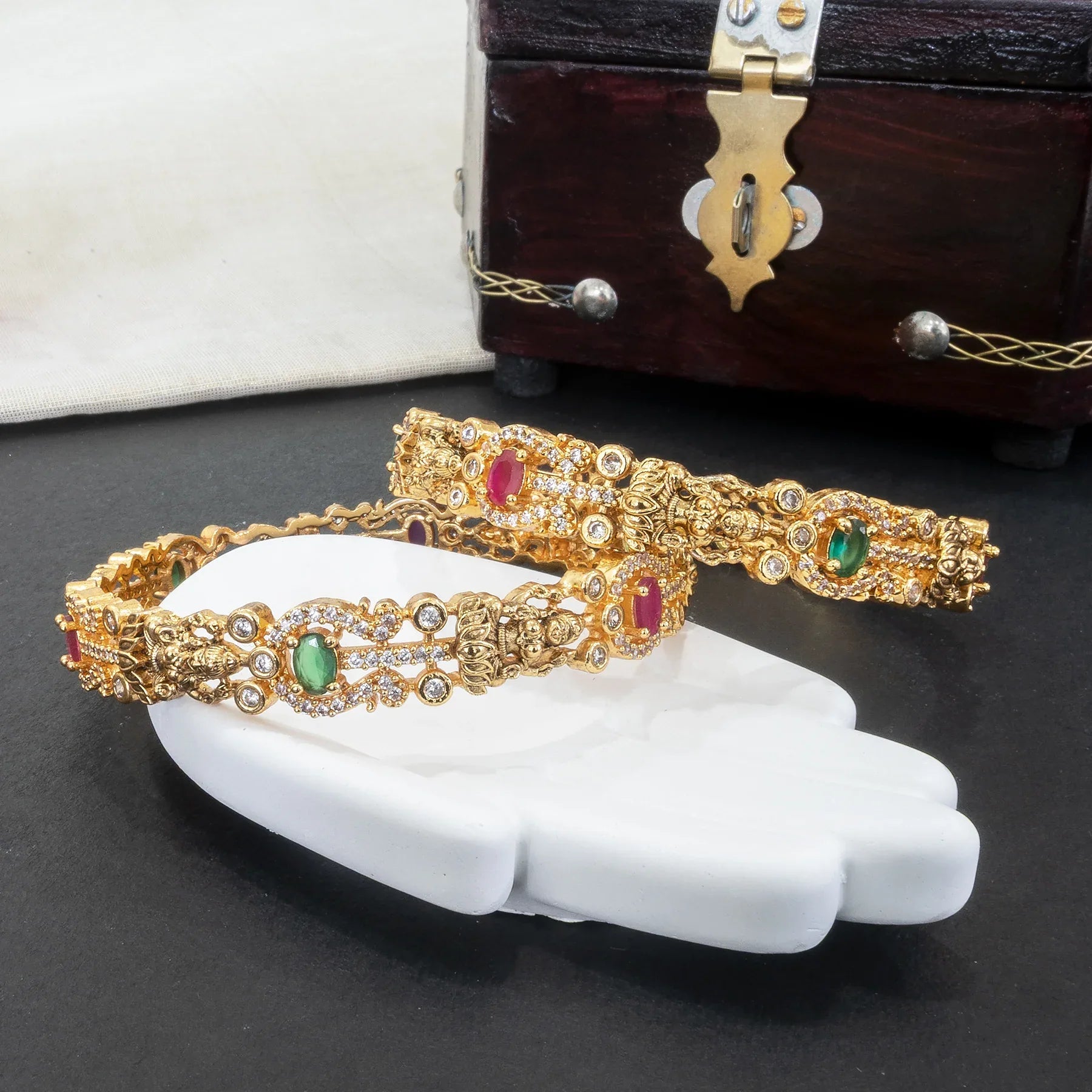 Gold bangles with gemstones on a white hand model against a dark background