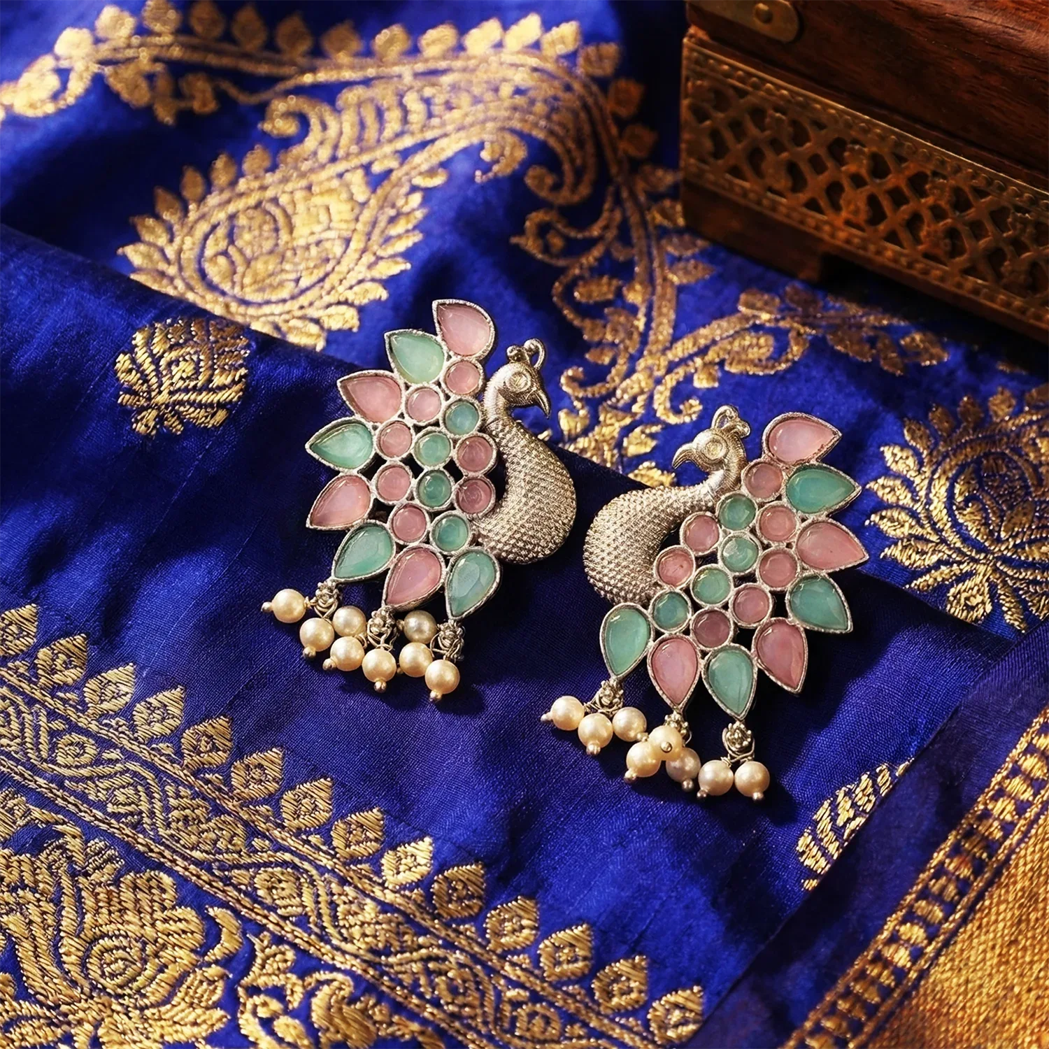 Decorative peacock earrings on a blue fabric with gold patterns