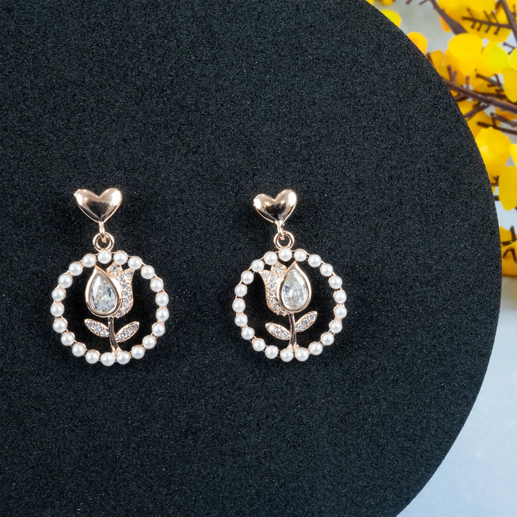 Pair of earrings with heart and floral design on a black stand.