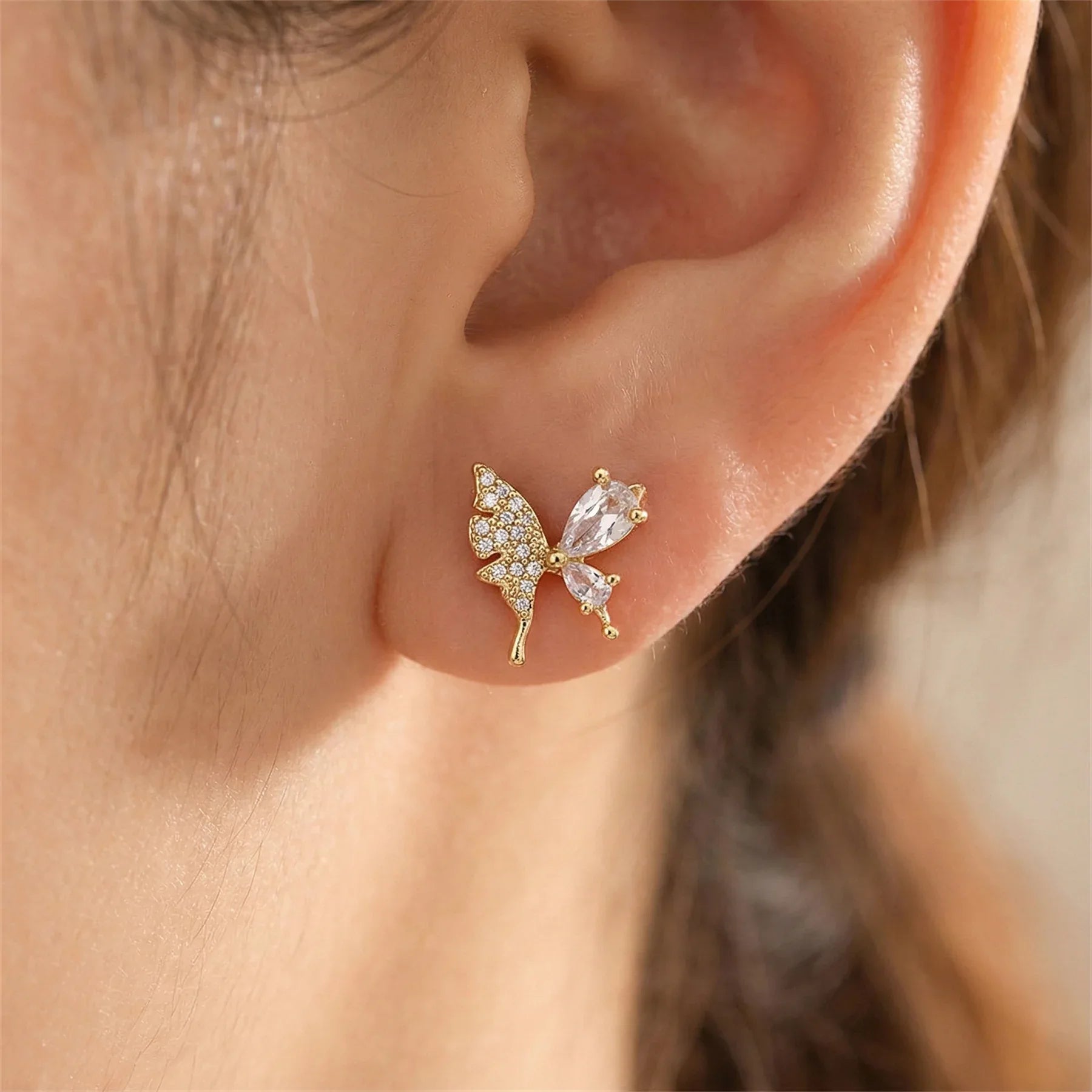 Gold butterfly earrings with gemstones worn by a person