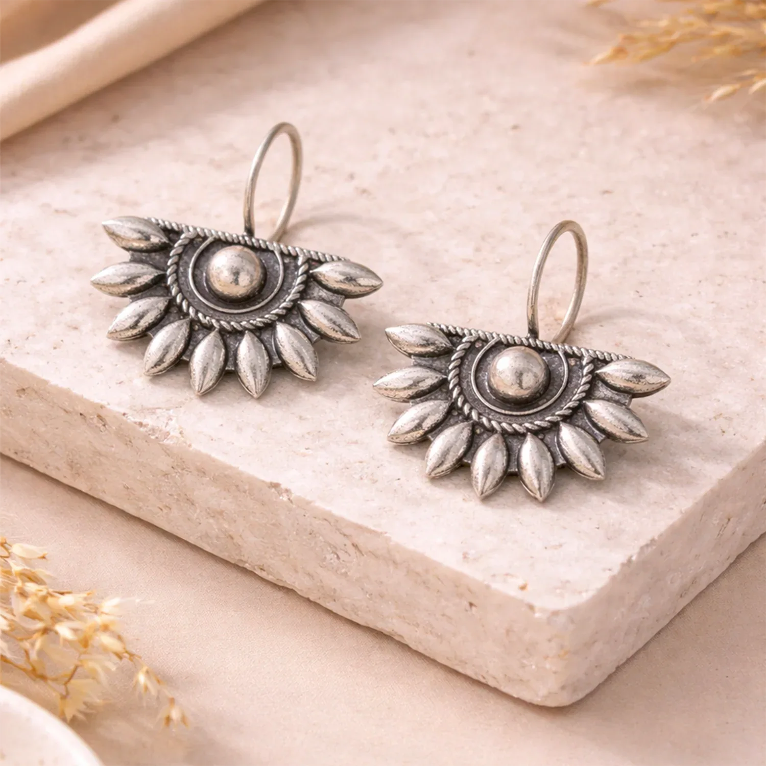 Pair of silver earrings on a light stone surface with dried flowers.