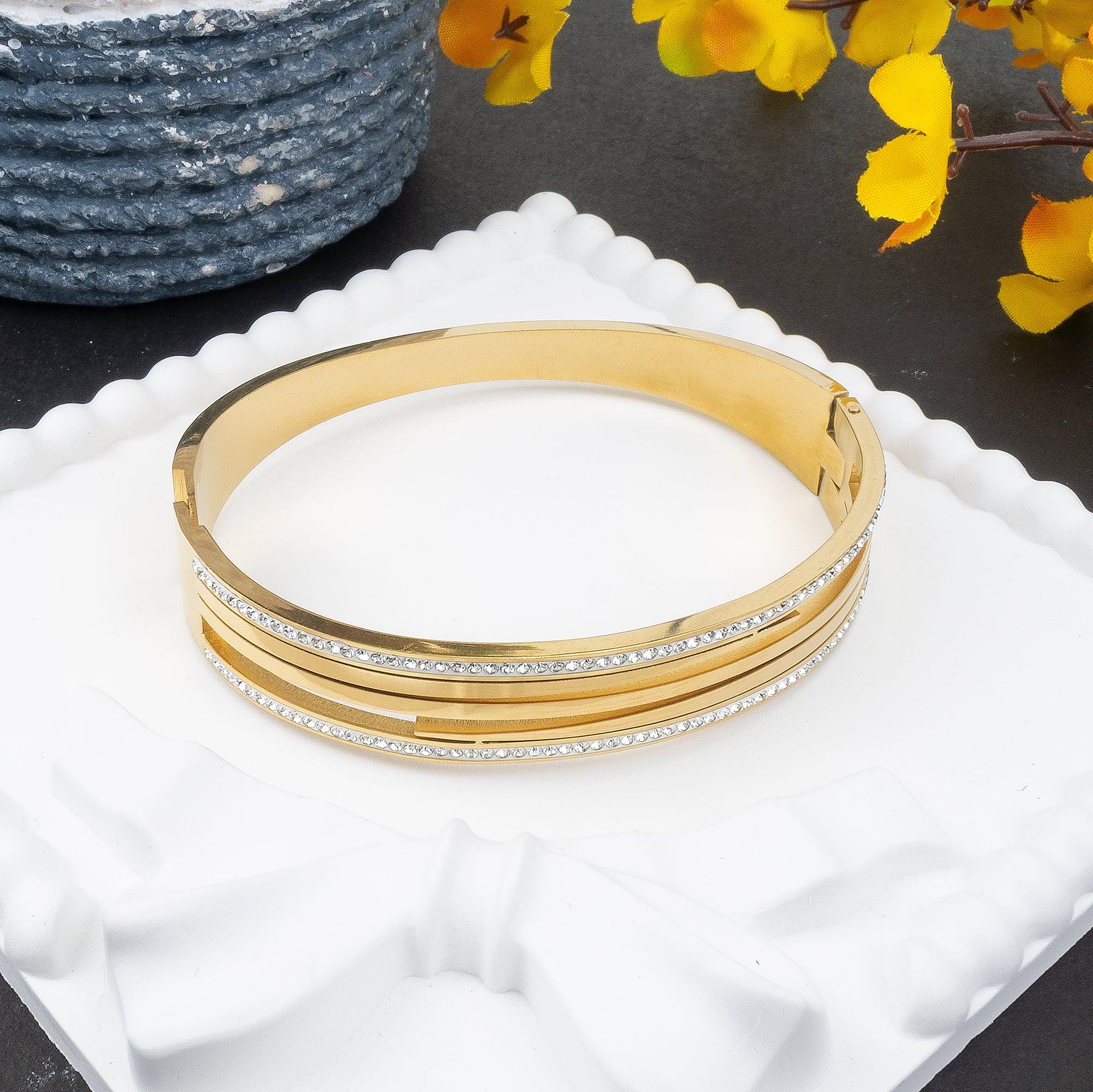 Gold bangles with crystals on a white surface with yellow flowers in the background