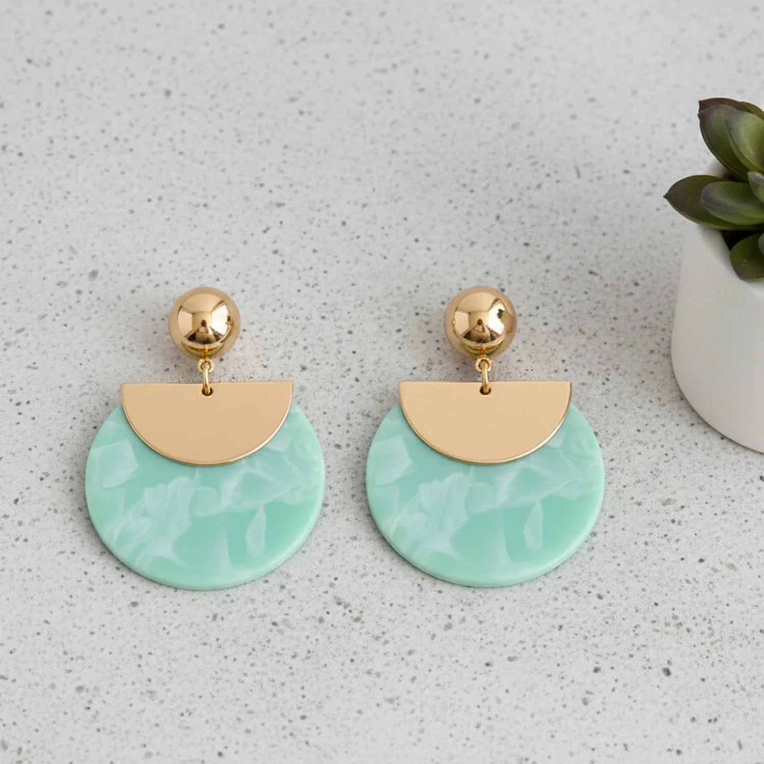 Pair of earrings with gold half-circle and green round design on a light gray surface.