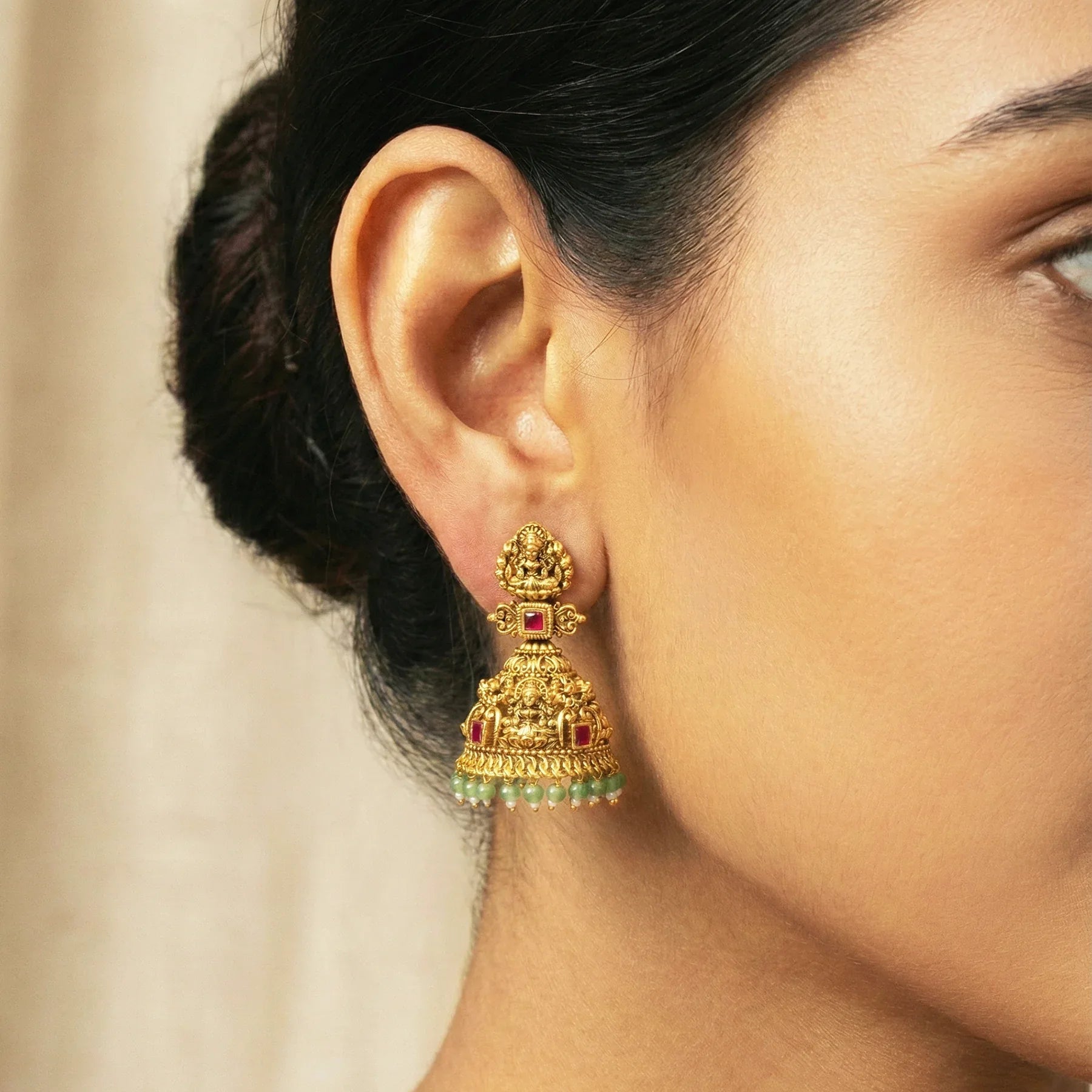 Gold earrings with green and red stones worn by a person