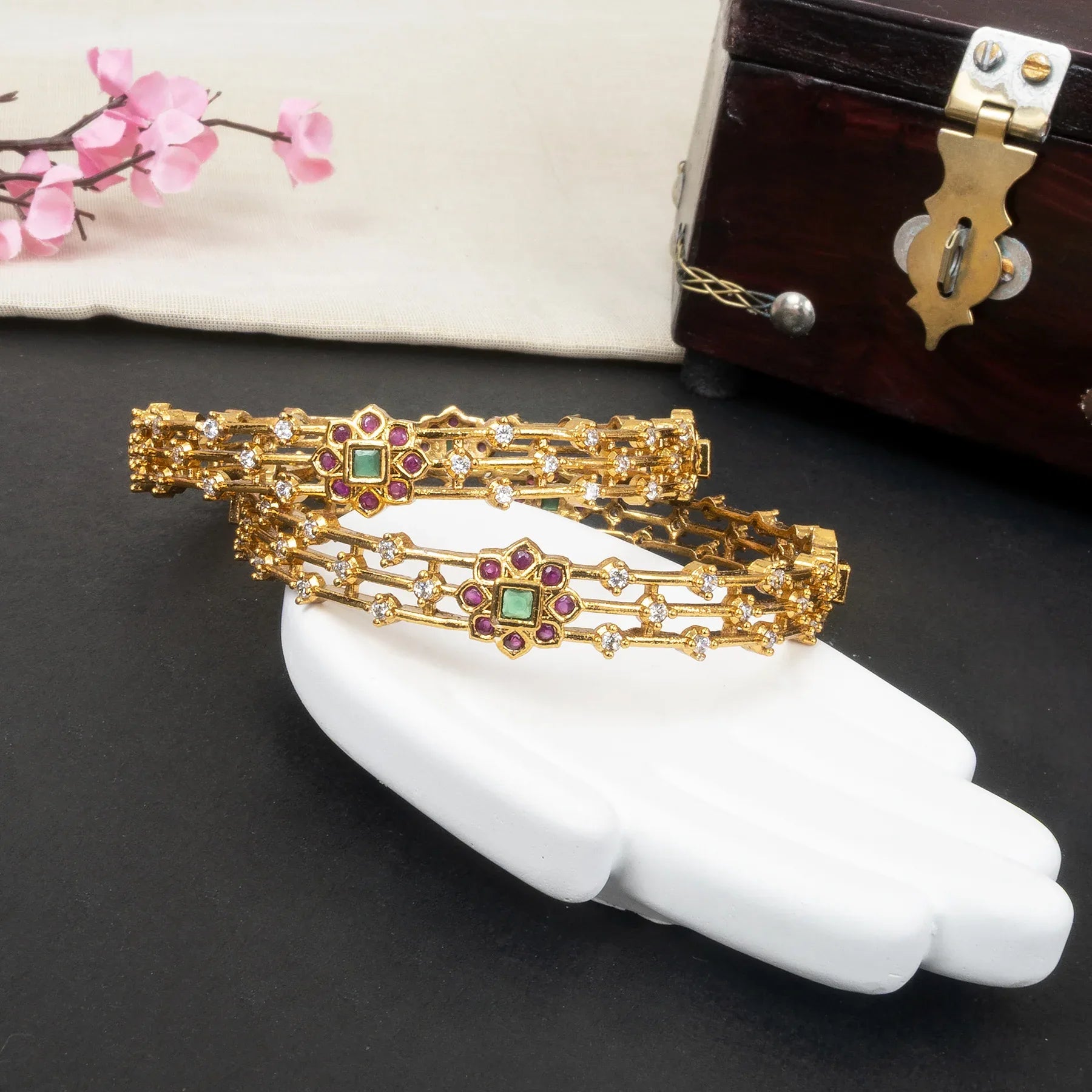 Gold bracelets with gemstones on a white hand model against a dark background