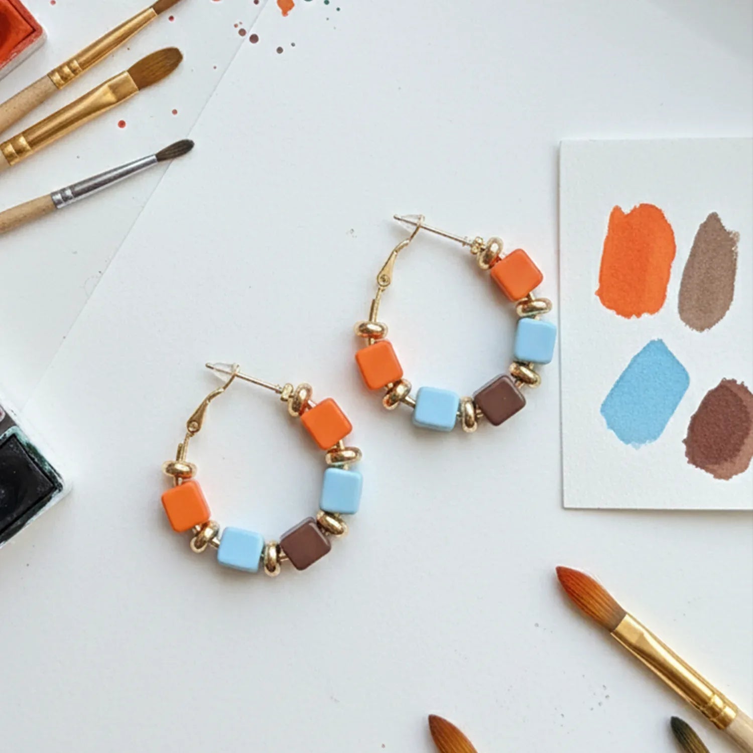 Colorful hoop earrings on a white surface with paintbrushes and color swatches.