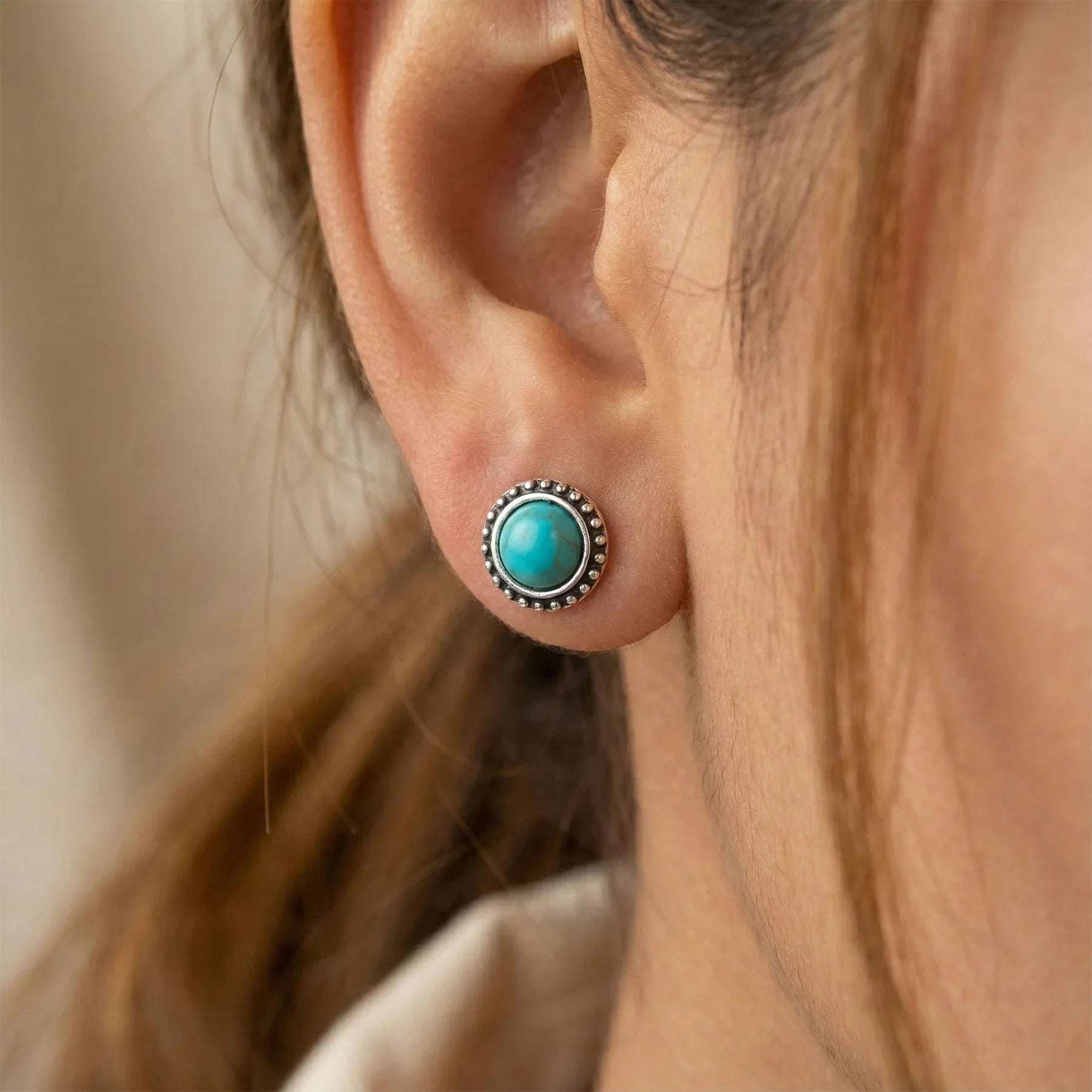 Close-up of an ear wearing a turquoise stud earring with a silver setting.