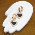 Heart-shaped earrings with gold and blue design on a white stand against a brown background