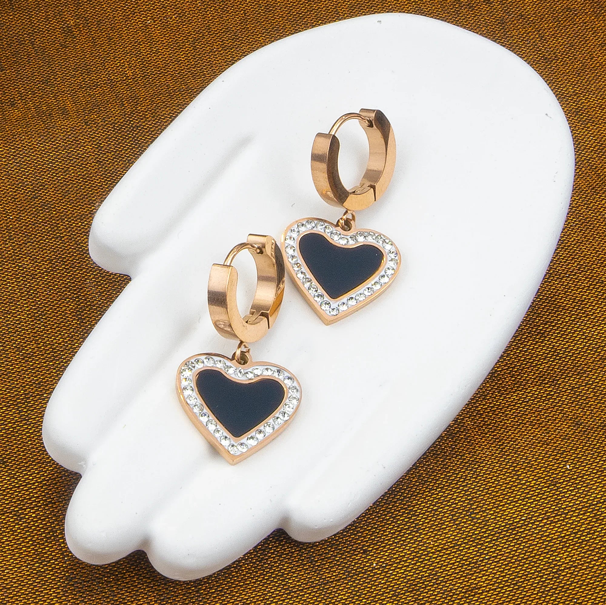 Heart-shaped earrings with gold and blue design on a white stand against a brown background