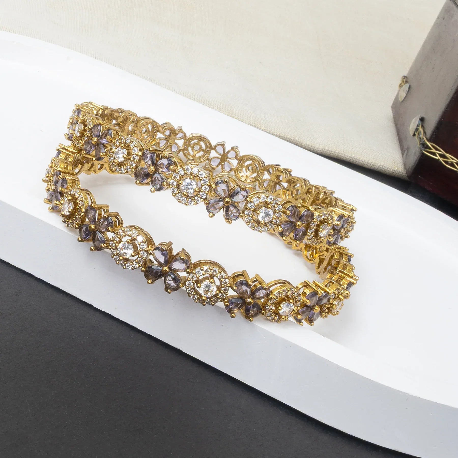 Gold bracelet with purple and clear gemstones on a white surface