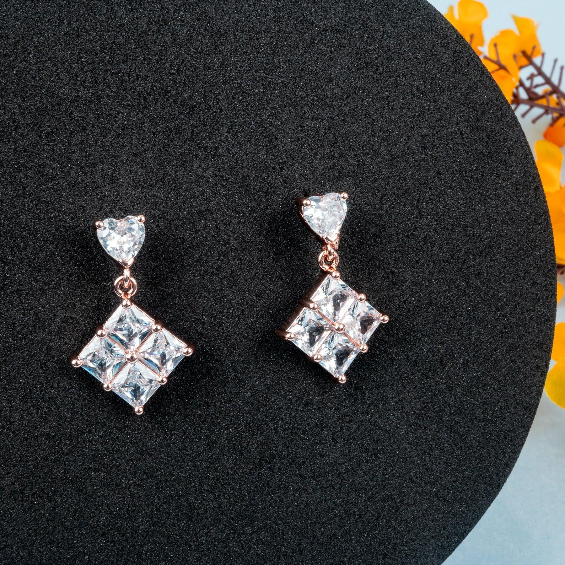 Pair of square-shaped earrings with rose gold accents on a black stand.