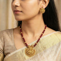 Woman wearing gold jewelry with a maroon necklace and earrings.
