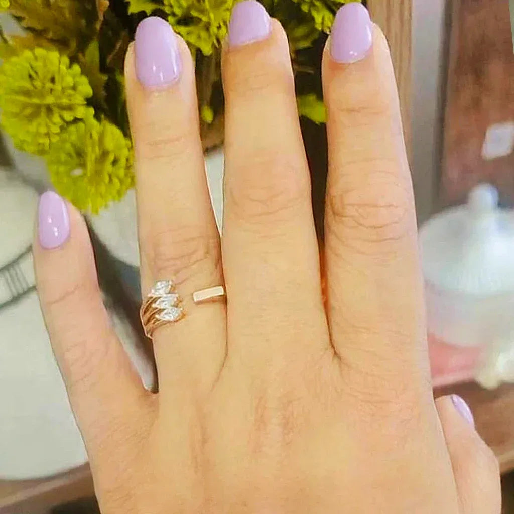 Hand with pink nail polish wearing a gold ring against a blurred floral background