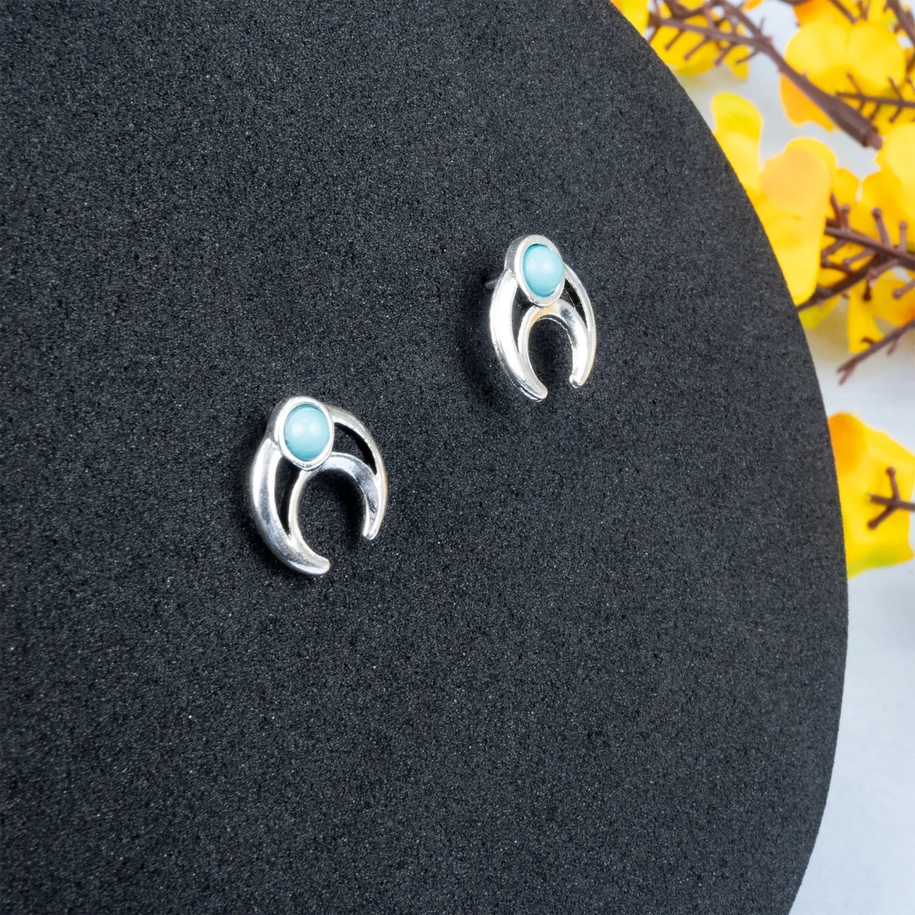 Silver earrings with turquoise stones on a black stand with yellow flowers in the background