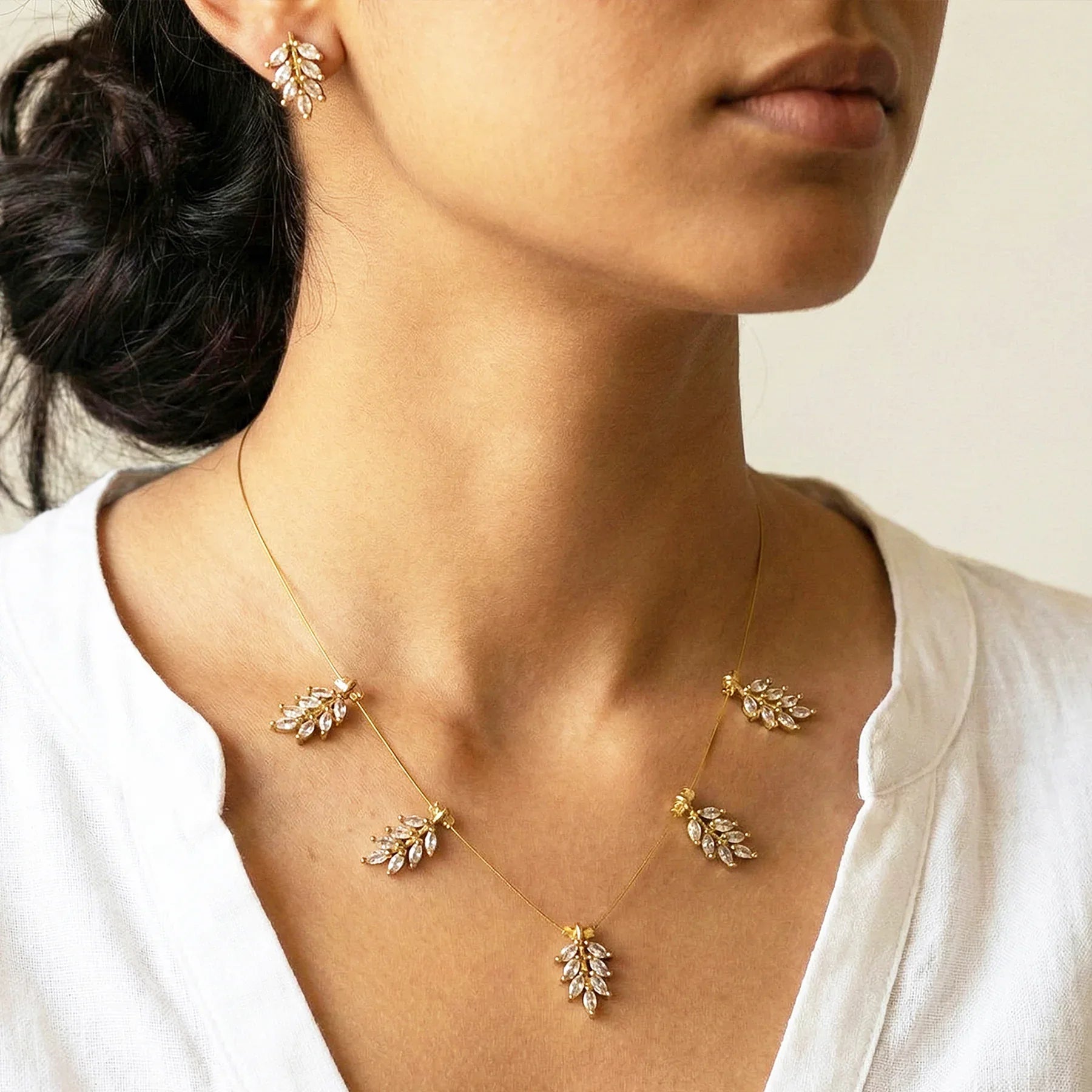 Woman wearing a delicate gold necklace and earrings with a neutral background