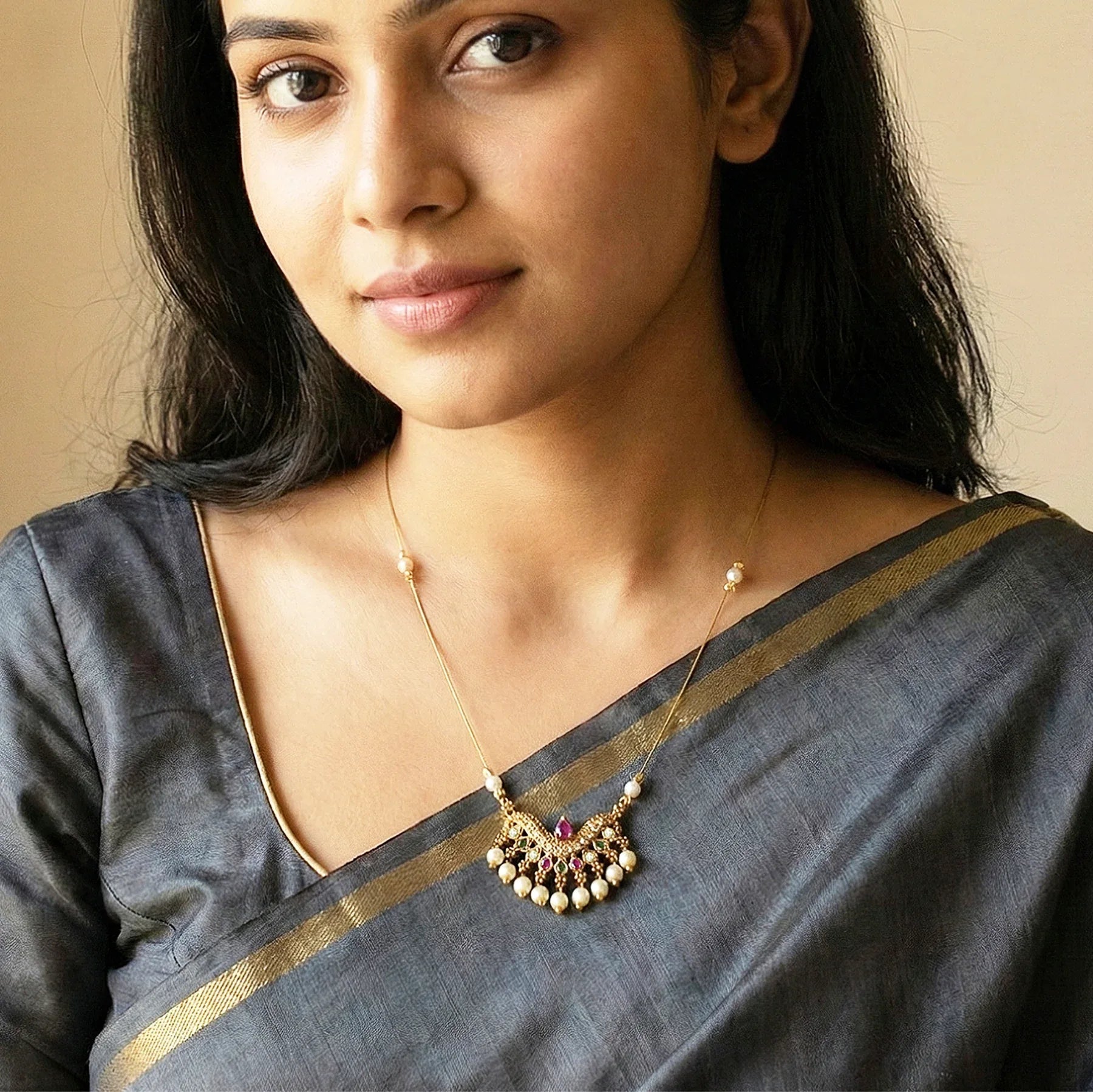 Woman wearing a traditional saree with a necklace against a beige background