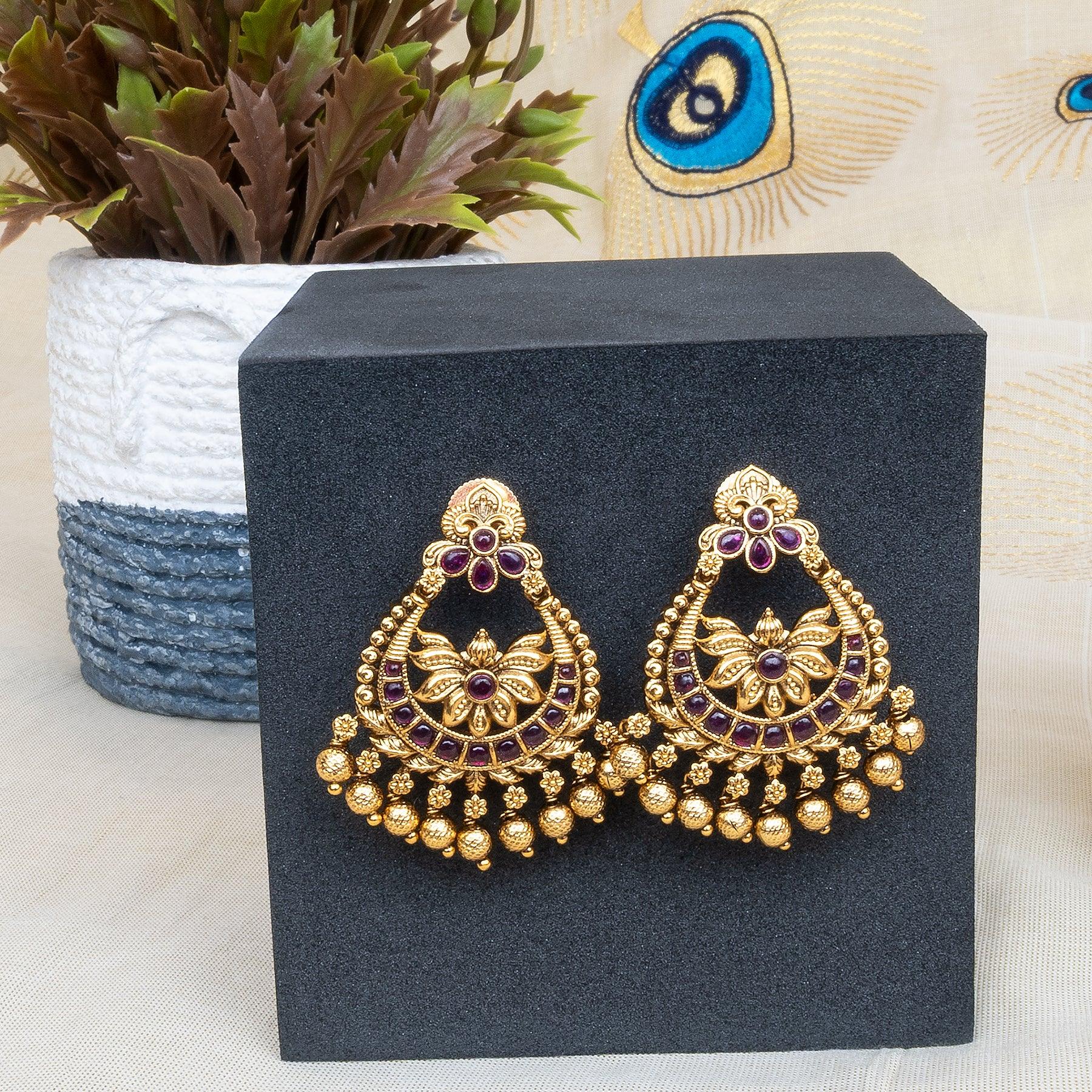 Gold earrings with purple stones on a black stand with a plant in the background
