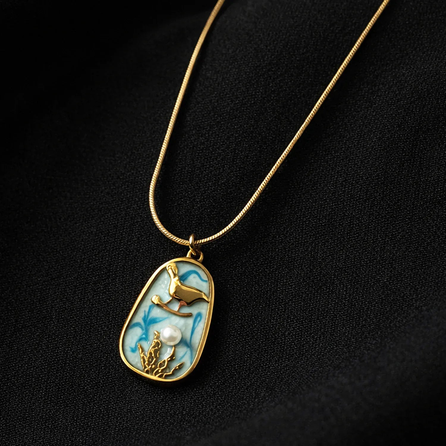 Gold necklace with a pendant featuring a deer and pearl on a black background