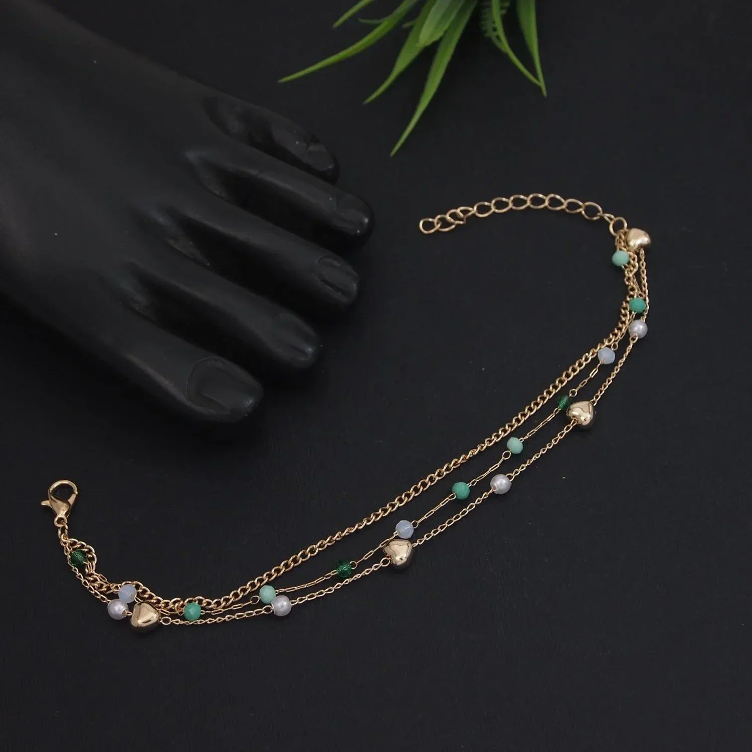 Gold necklace with green and white beads on a black background