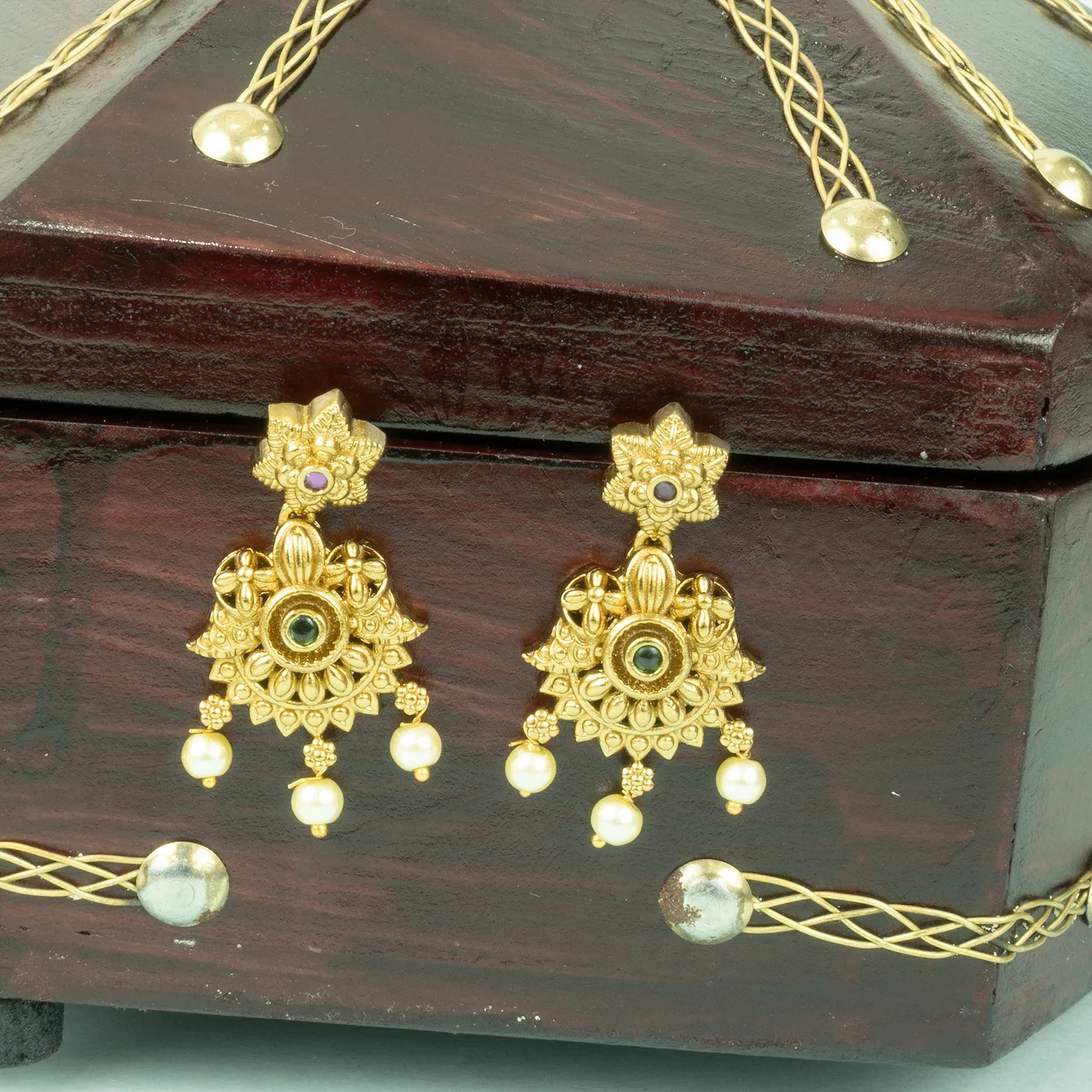 Gold earrings with floral designs on a wooden jewelry box