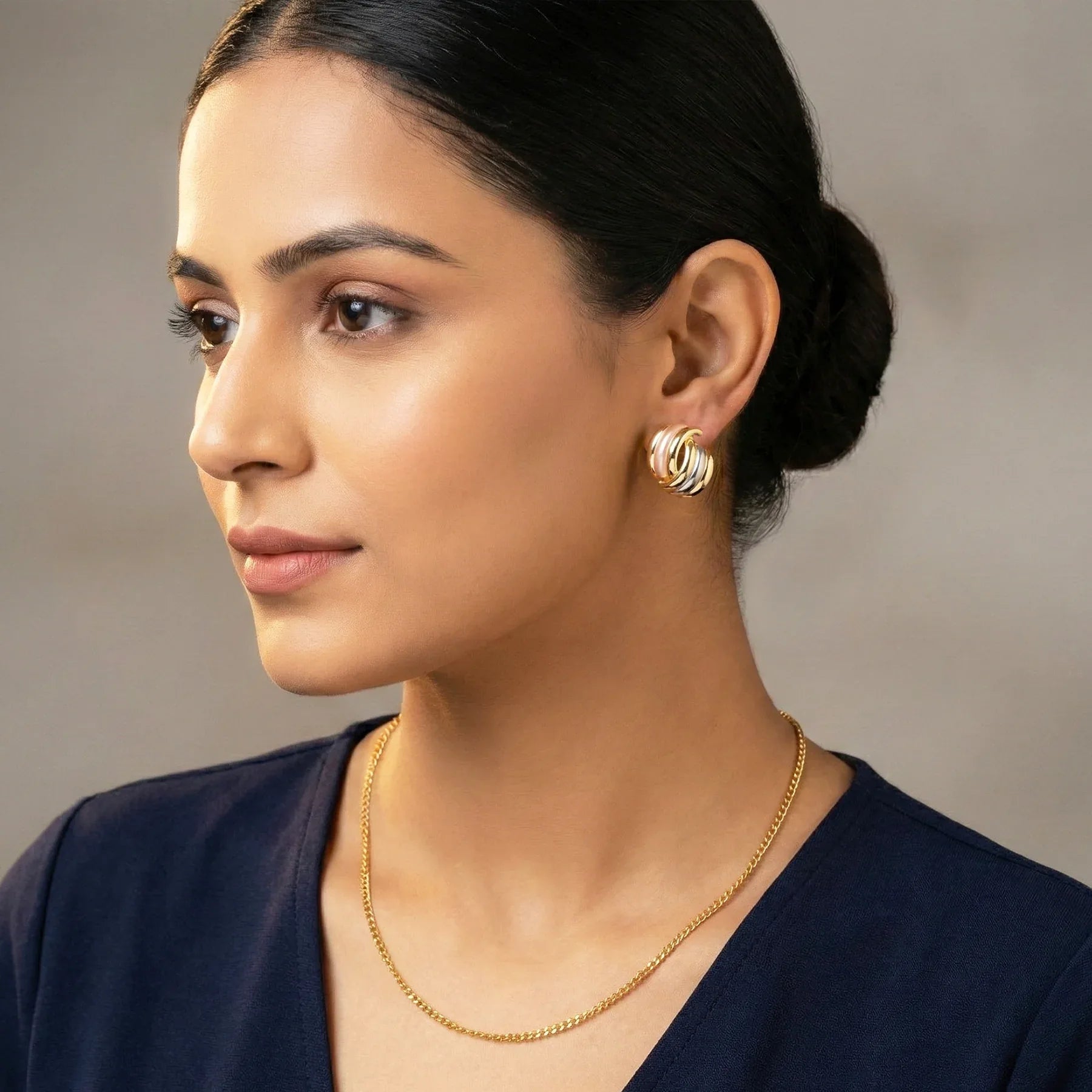 Woman wearing gold earrings and necklace against a neutral background