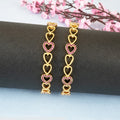 Gold heart-shaped earrings with pink gemstones on a dark surface with pink flowers in the background.