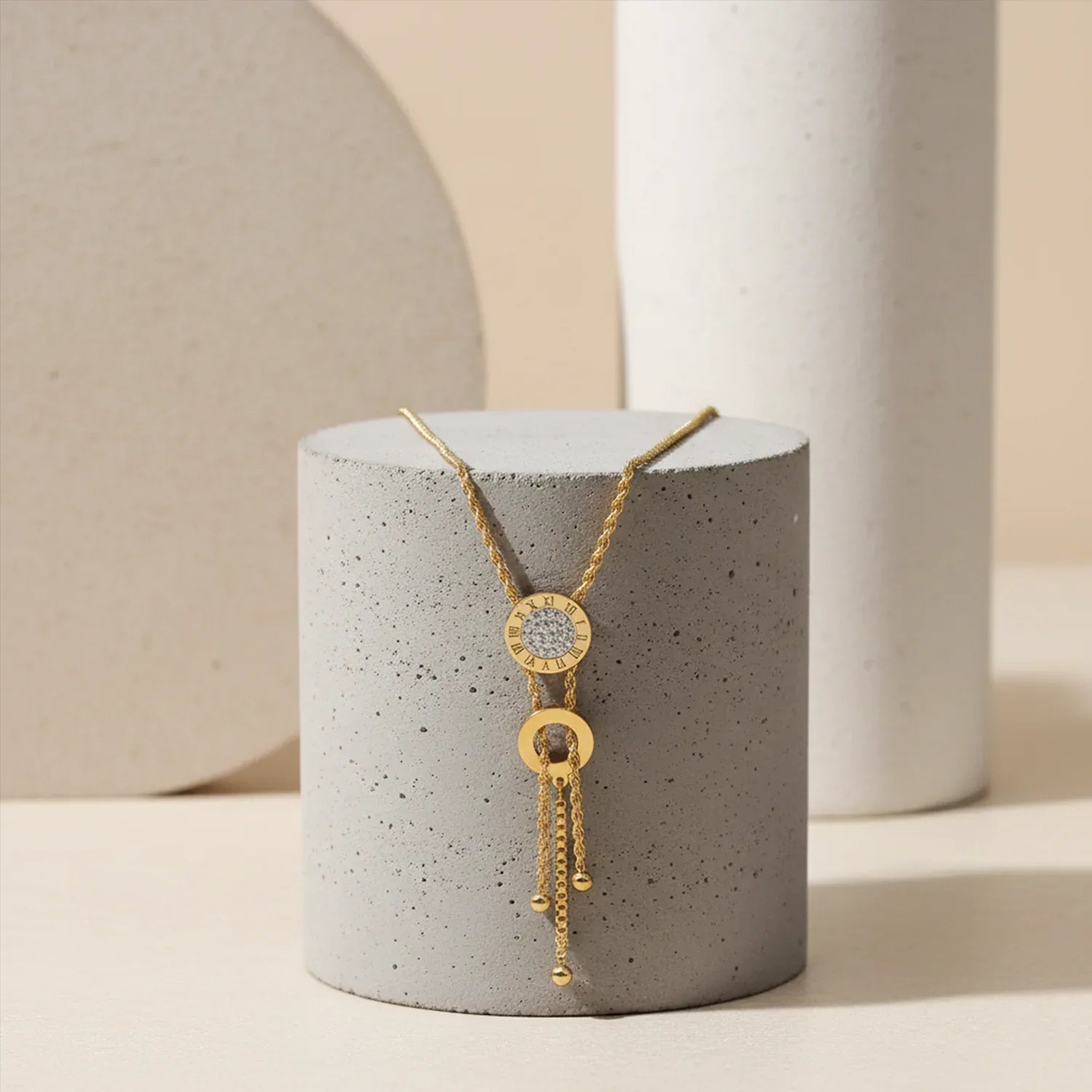 Gold necklace with a pendant on a gray cylindrical stand against a neutral background