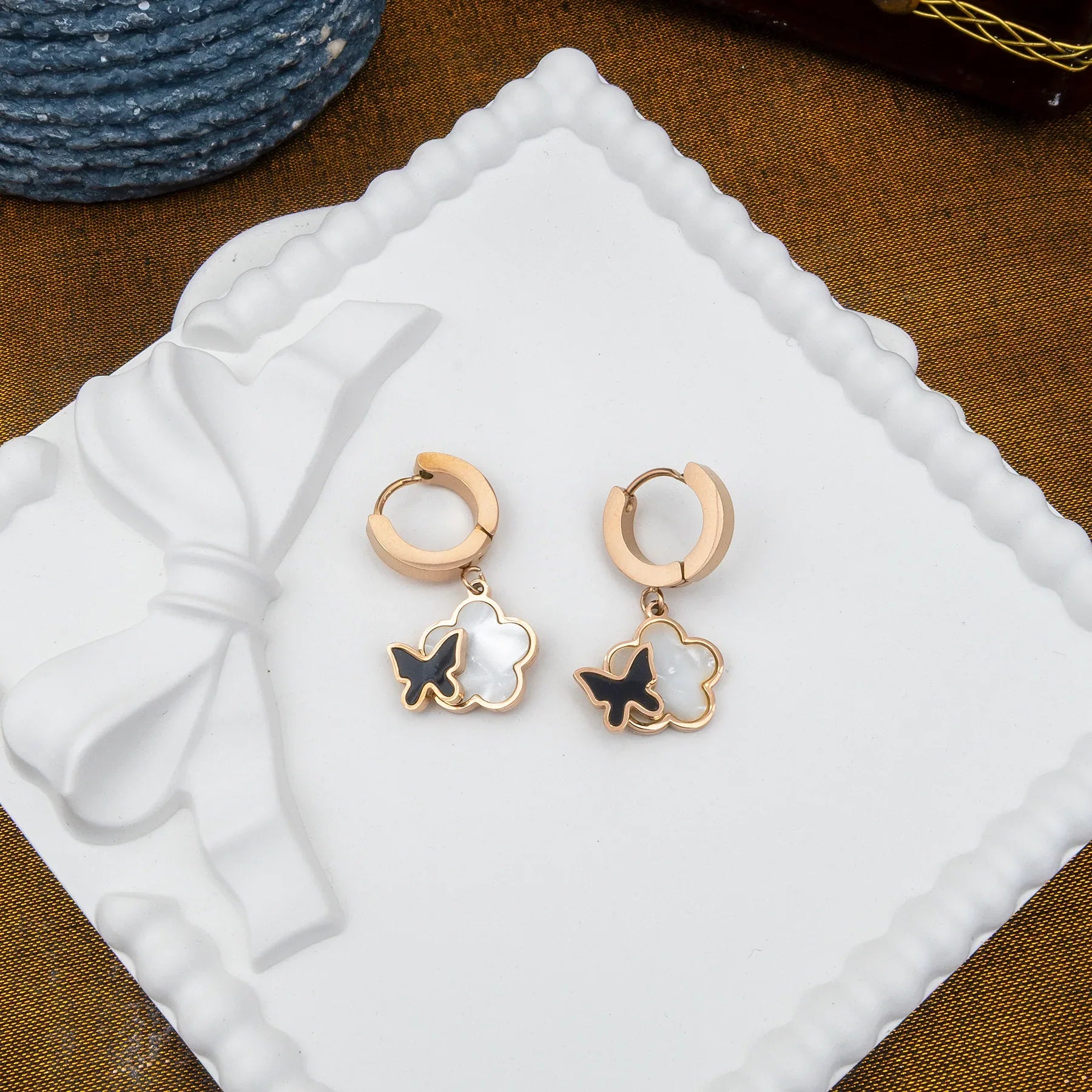 Rose gold earrings with butterfly designs on a white cushion