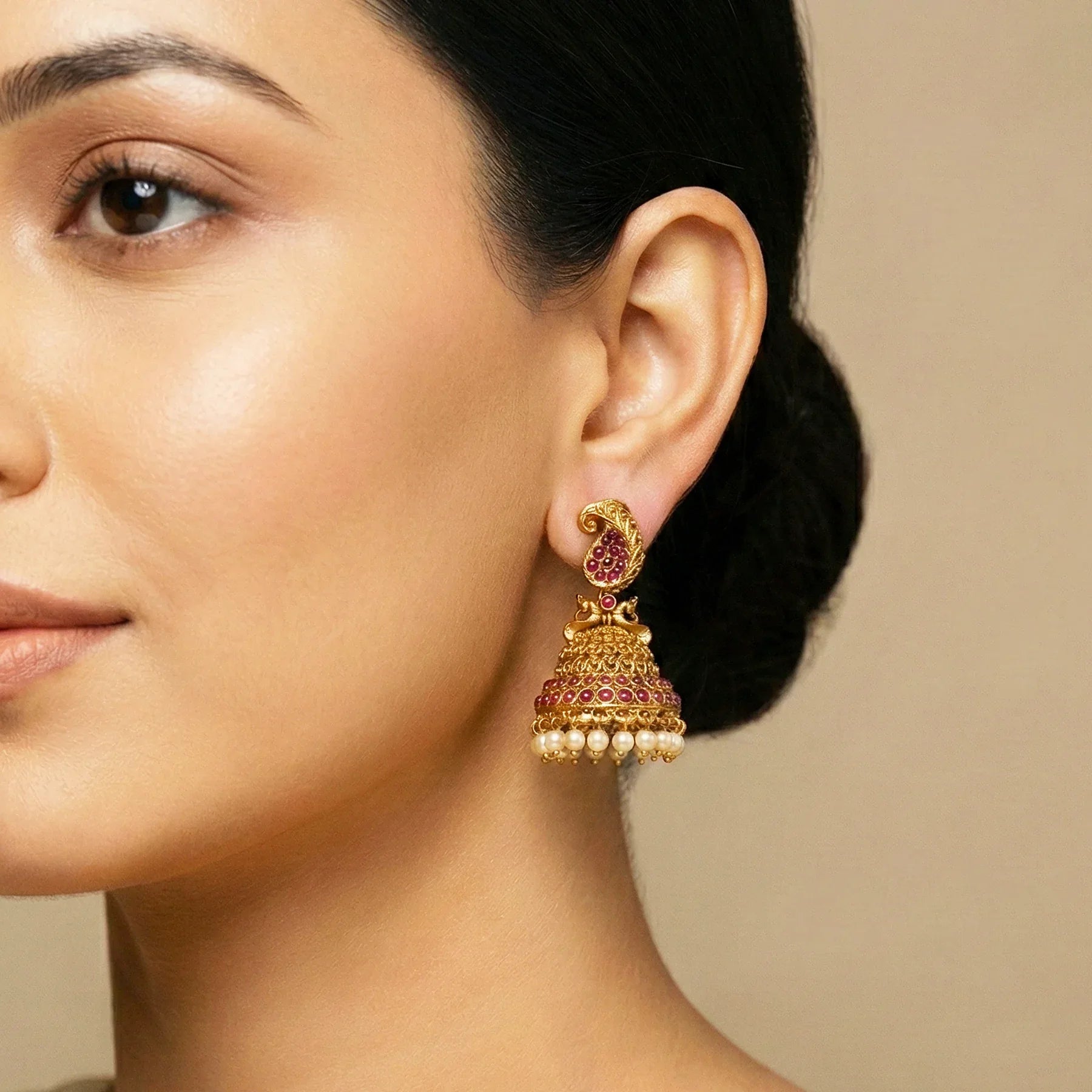 Close-up of a woman wearing a gold and red earring against a beige background
