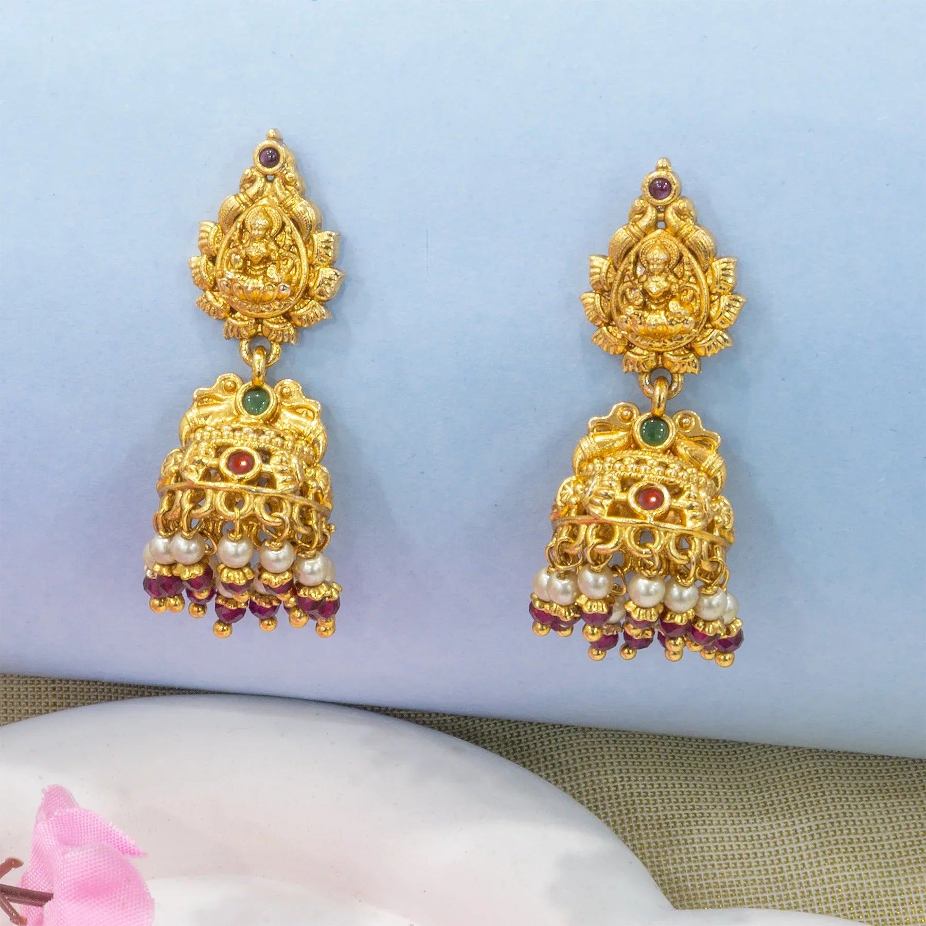 Gold earrings with pearls and gemstones on a light blue background