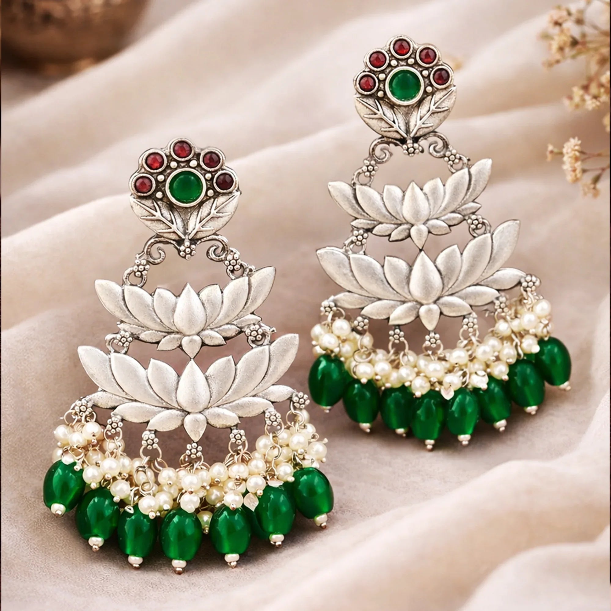 Ornate earrings with green and red stones on a soft fabric background