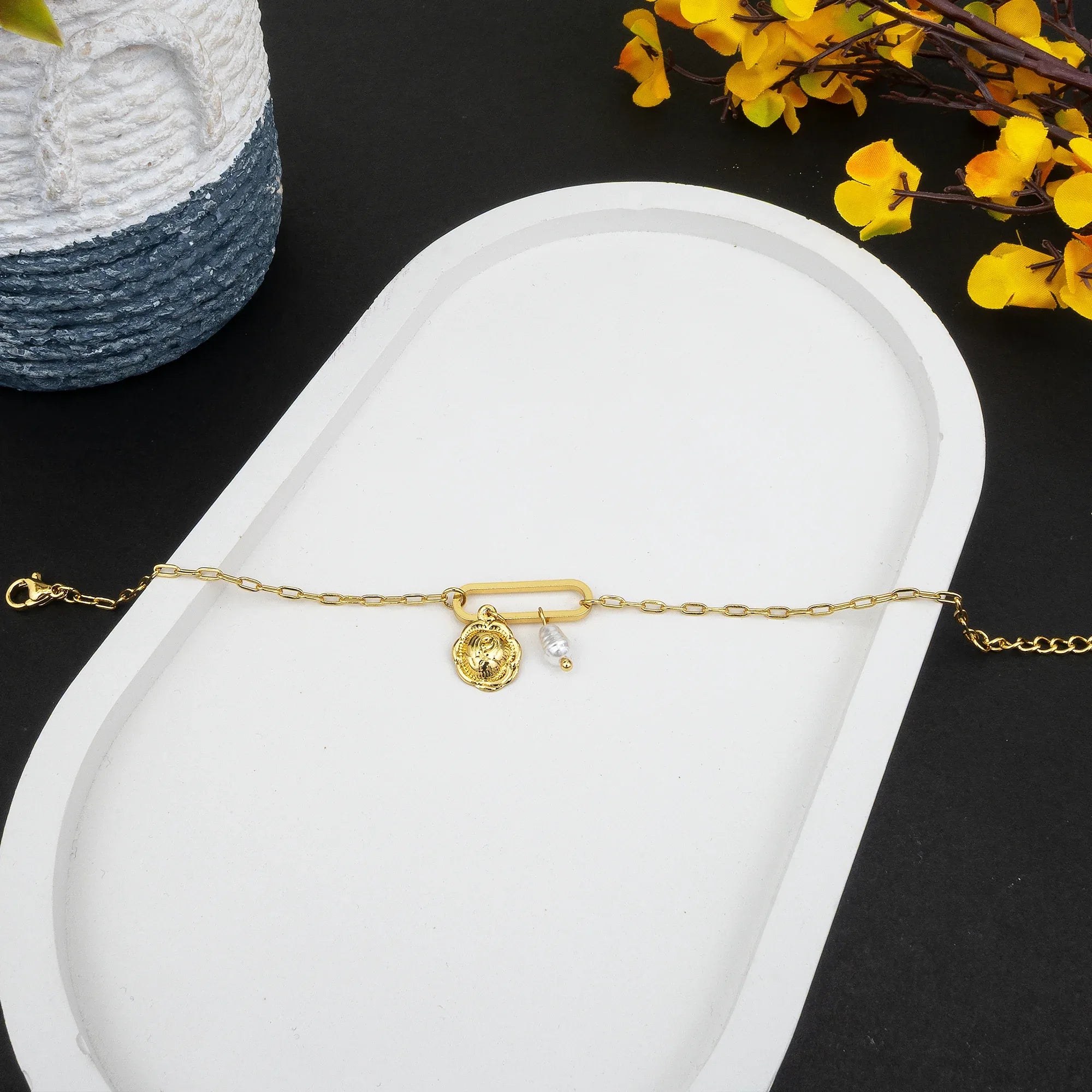 Gold bracelet with a heart charm on a white tray with yellow flowers in the background