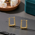 Gold hoop earrings on a dark surface with a wooden plate and teal box in the background.
