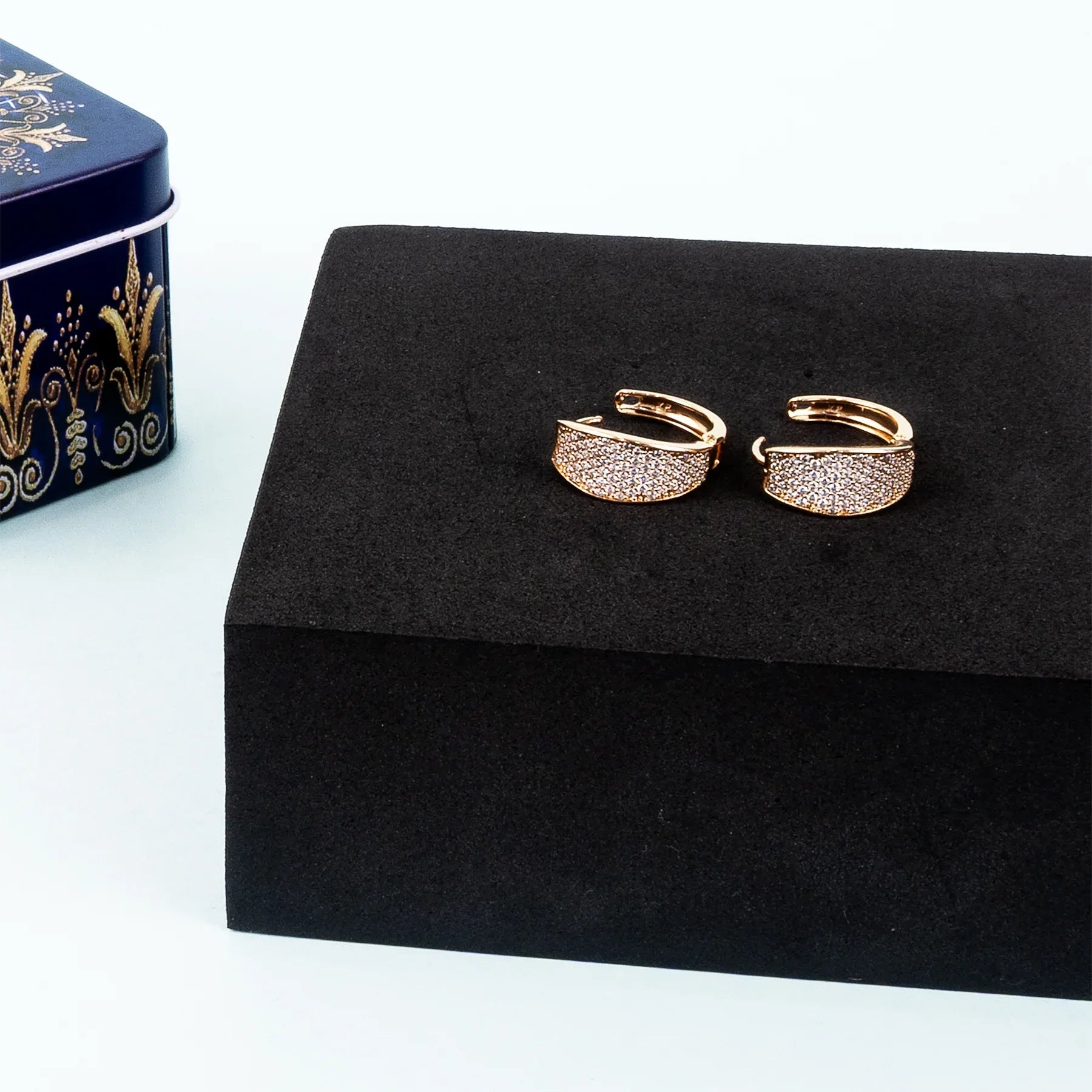 Gold hoop earrings on a black jewelry box with a decorative box in the background