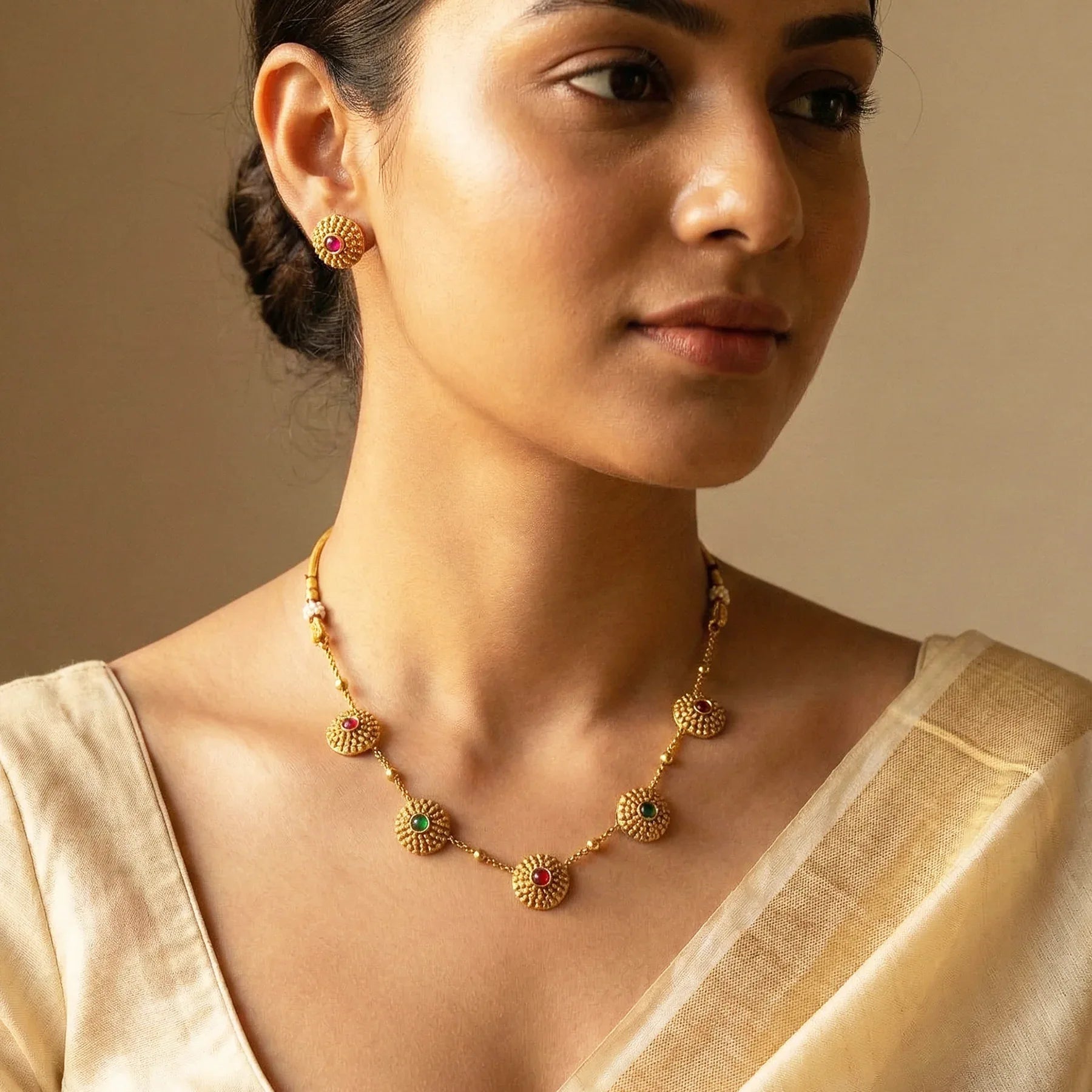 Woman wearing a gold necklace and earrings against a beige background